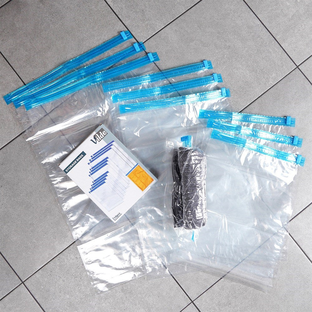 Bolsas de almacenamiento al vacío con cierres azules y un rollo de ropa en suelo de baldosas grises.
