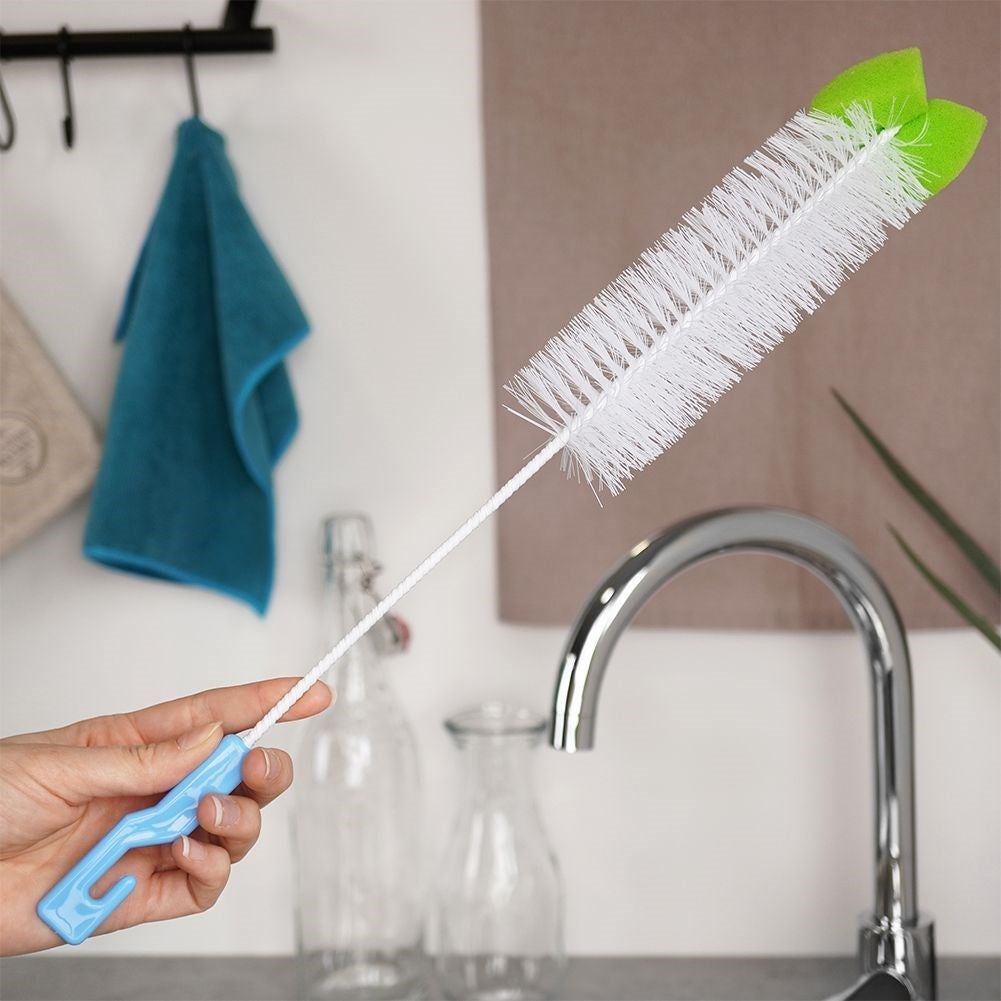 Una mano sostiene un cepillo blanco con mango azul y puntas de esponja verde.