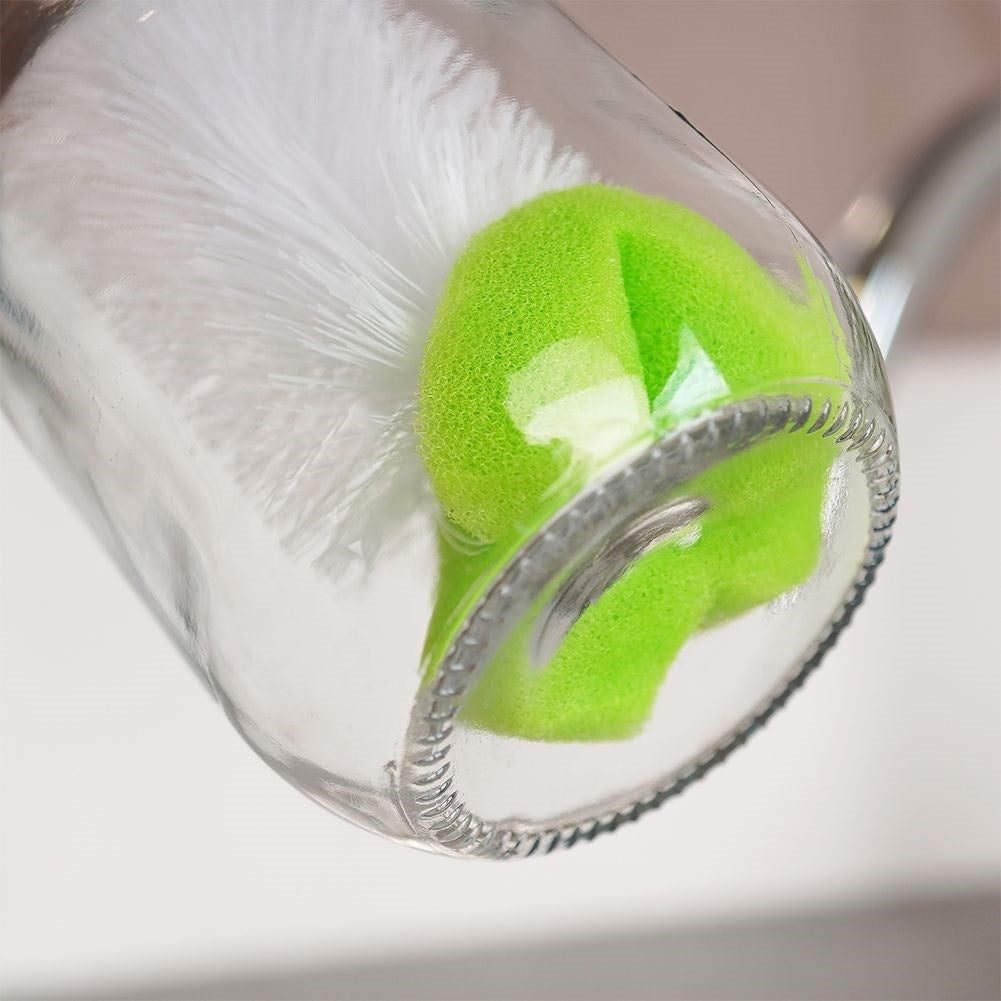 Un cepillo para botellas blanco y una esponja verde dentro de una botella de vidrio.
