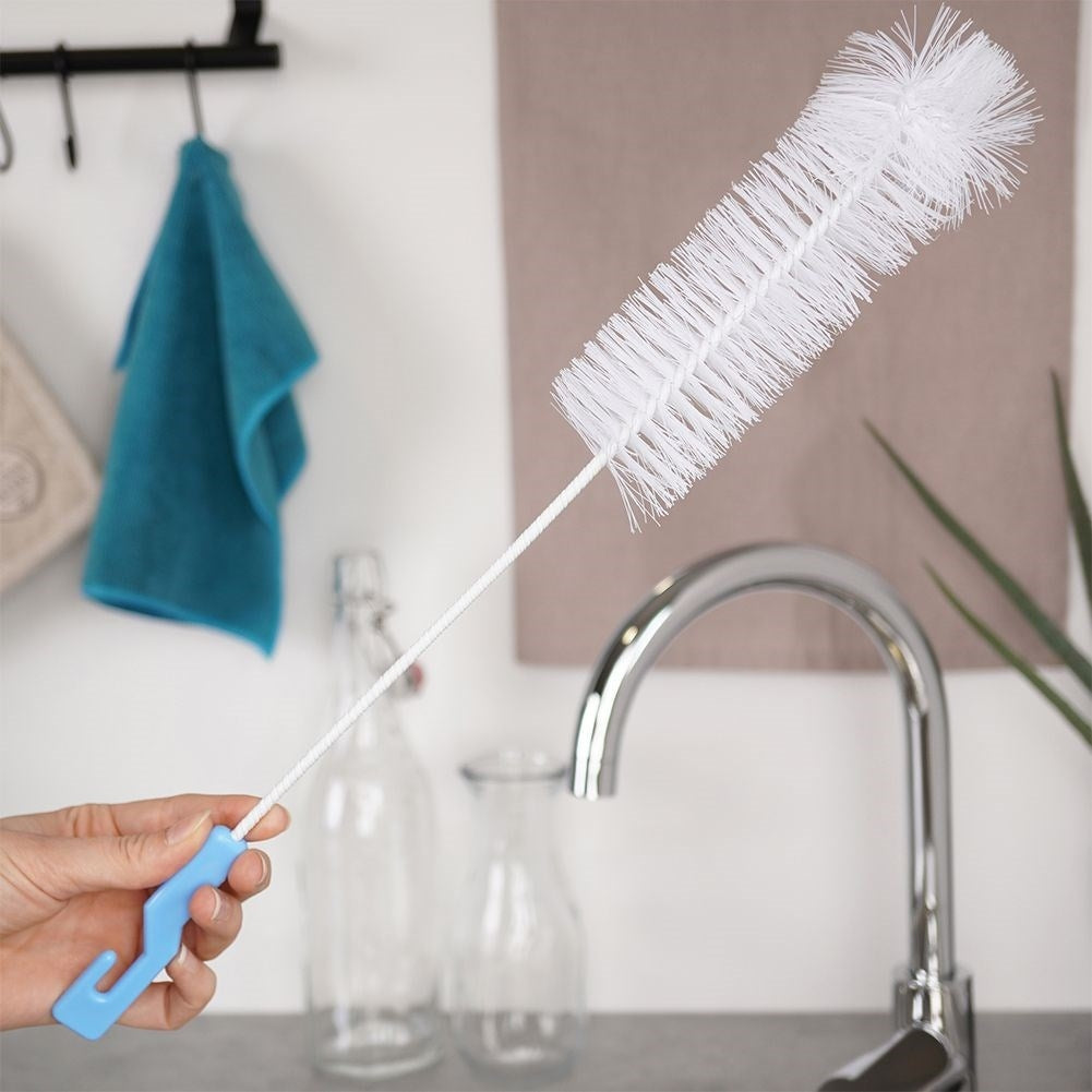 Un cepillo para botellas blanco con mango azul está junto a un fregadero y botellas de vidrio.