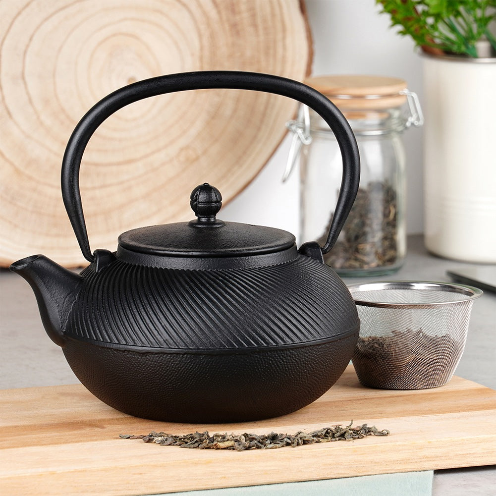 Tetera negra de hierro fundido con patrón acanalado, junto a un colador de té.
