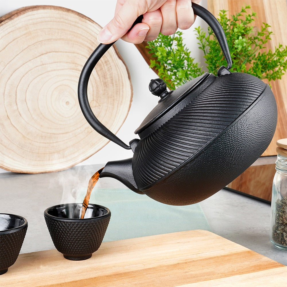 Una mano vierte té negro de una tetera en una taza pequeña.