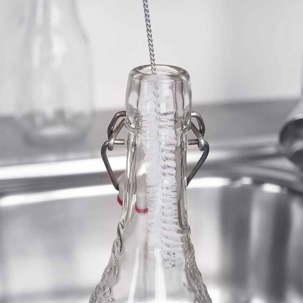 Cepillo para botellas limpiando el interior de una botella de vidrio con tapón abatible.