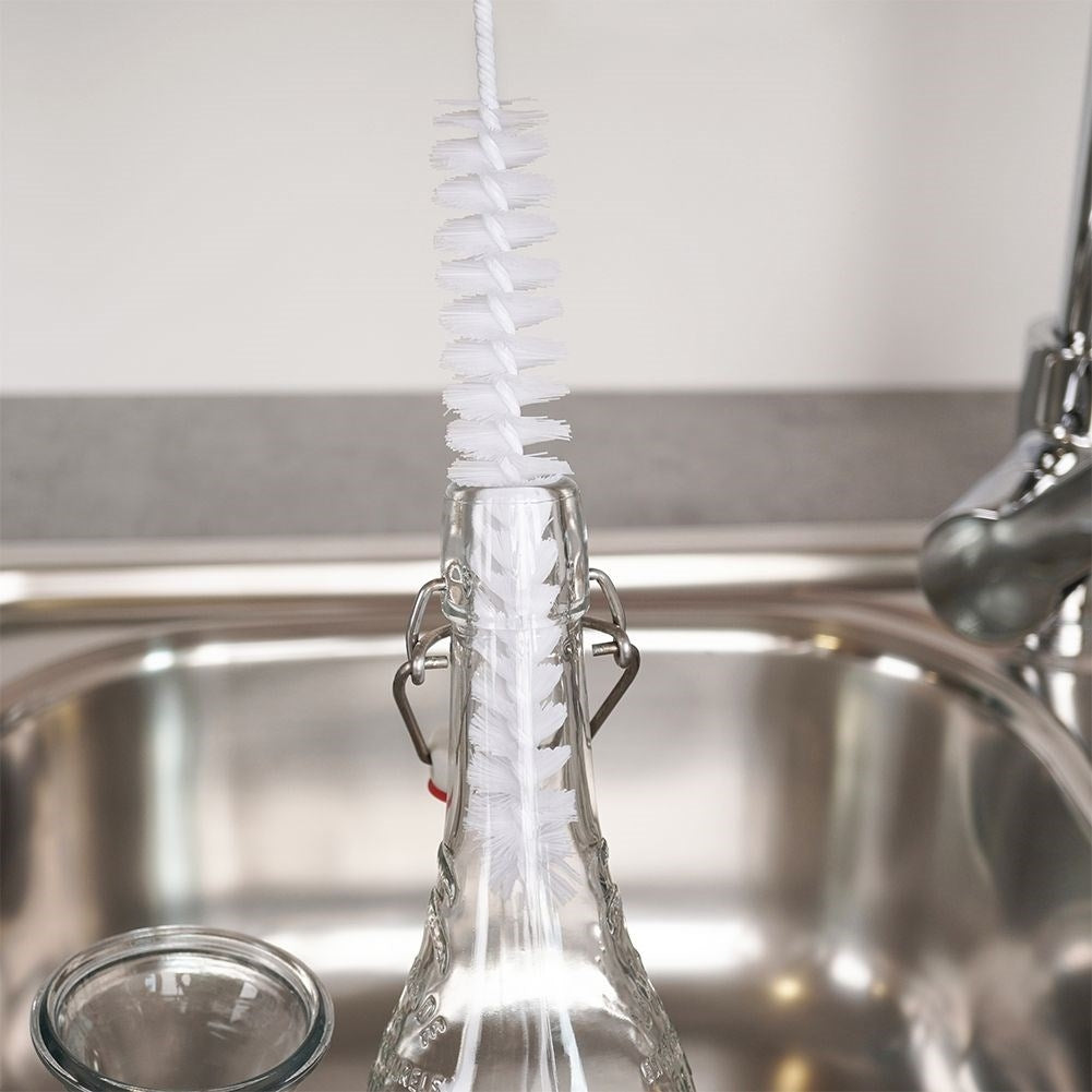 La cabeza de un cepillo para botellas blanco sobresale de una botella de vidrio en un fregadero.