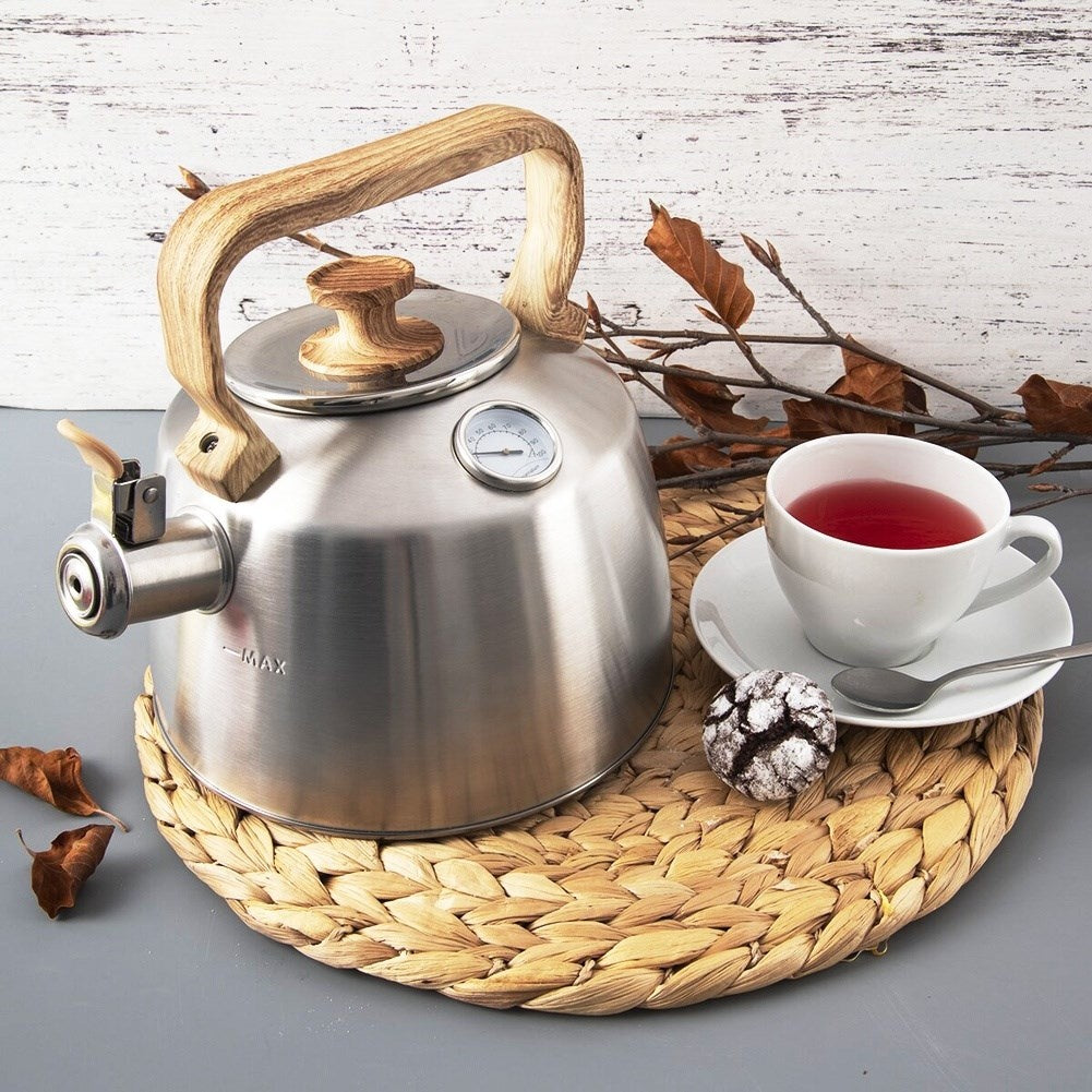 Una tetera plateada con asa de madera junto a una taza de té y una galleta.