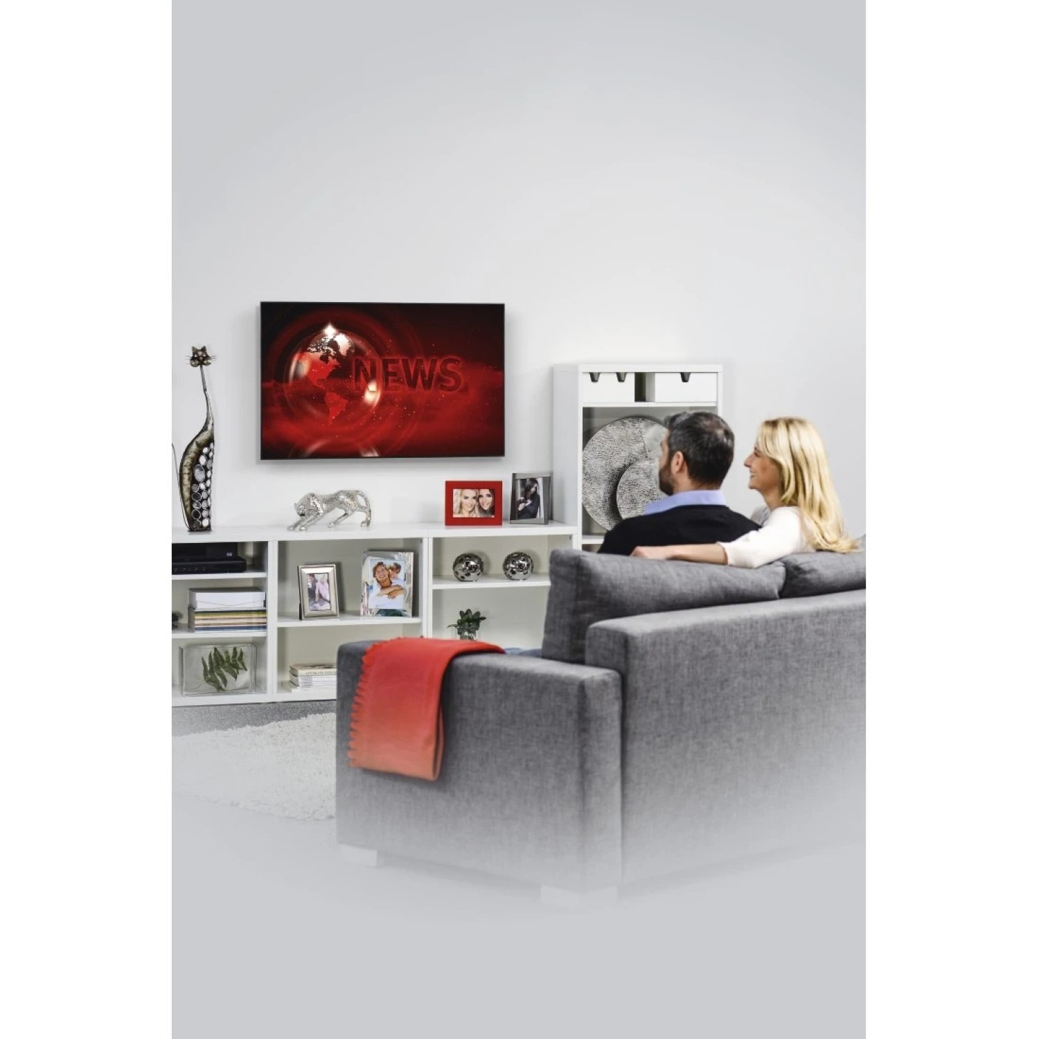Ein Paar sitzt auf einem Sofa und schaut fern. Nachrichten werden angezeigt.
