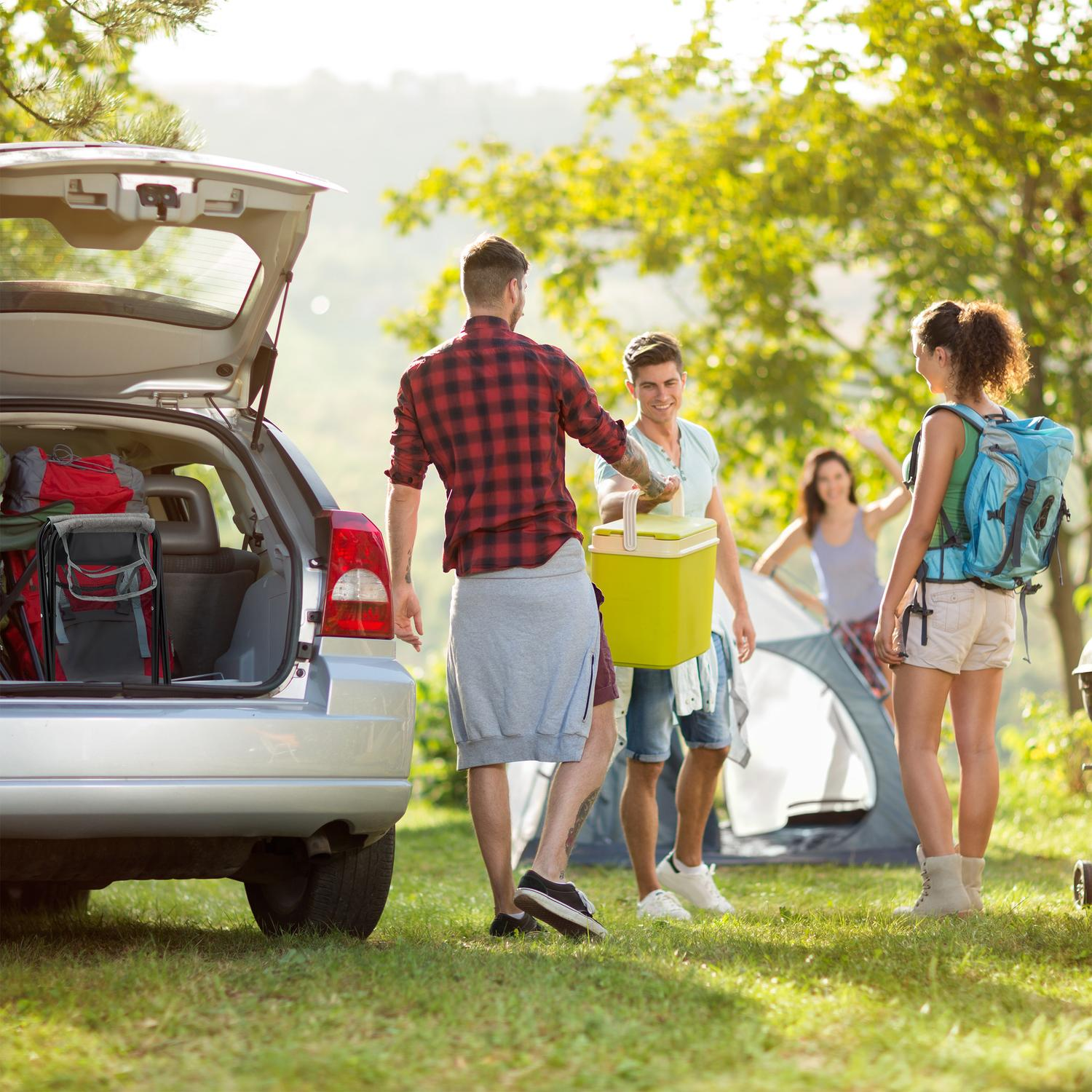 Gente descargando equipo de camping de un coche, con tienda de campaña atrás.