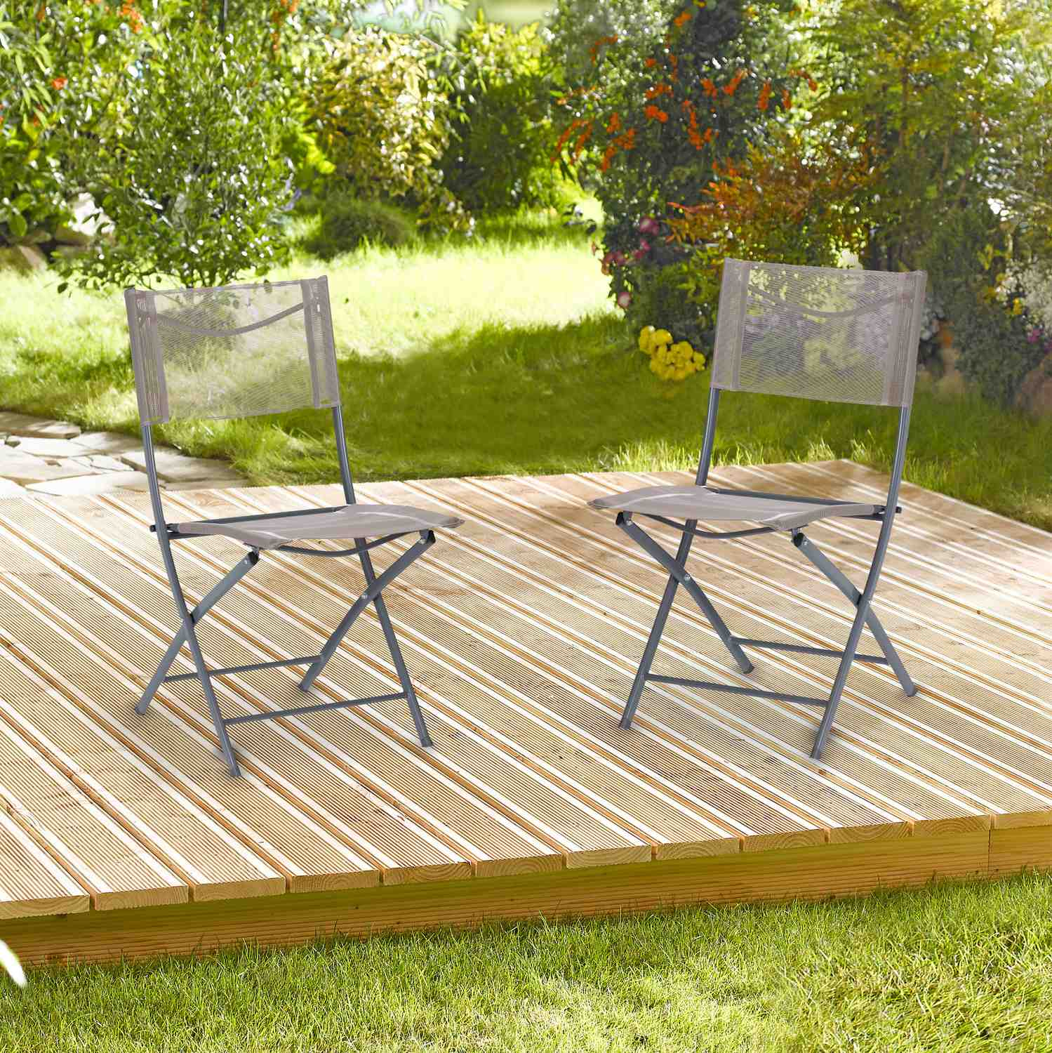 Dos sillas plegables grises sobre una terraza de madera con césped verde y arbustos detrás.