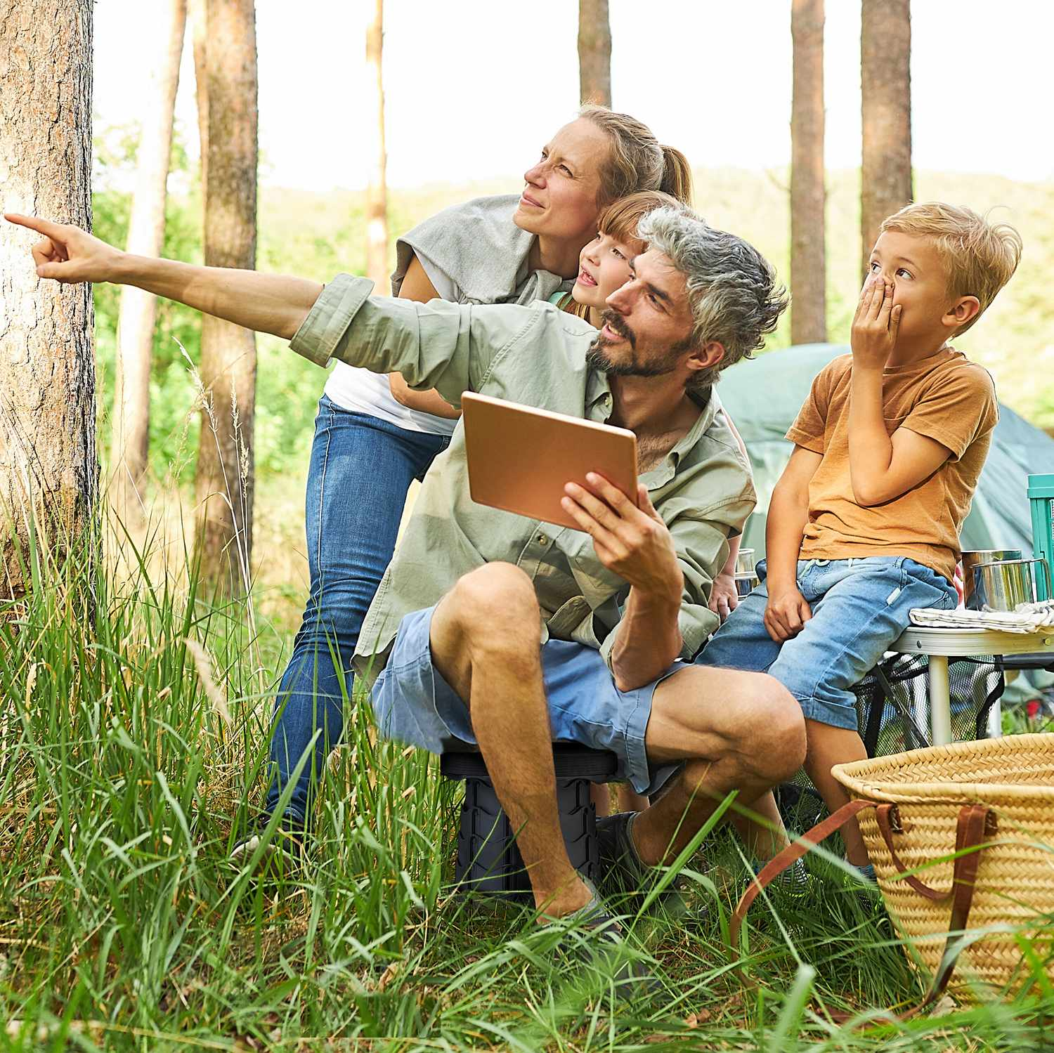 Familia señala algo en el bosque mientras sostiene una tablet. Acampando.