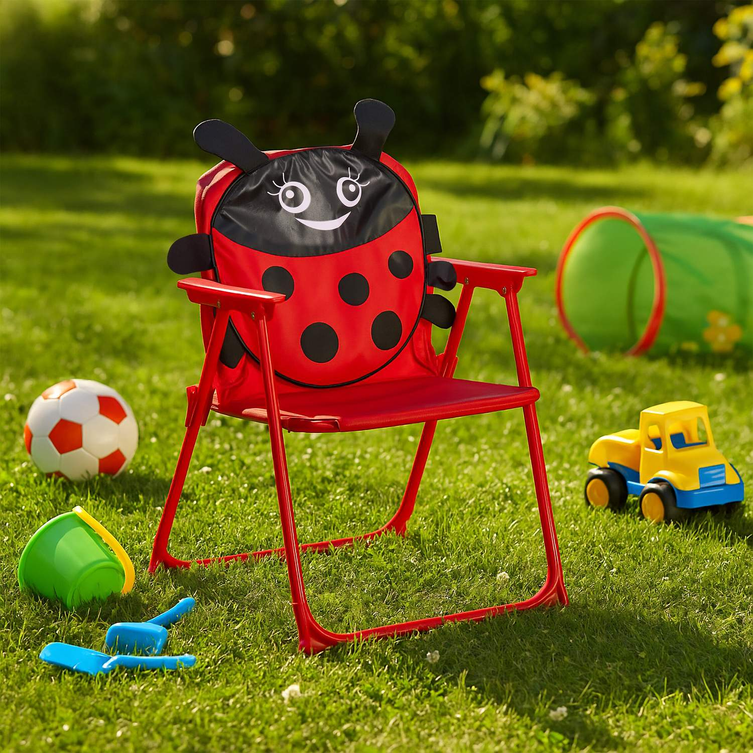 Silla roja de mariquita con juguetes en césped.