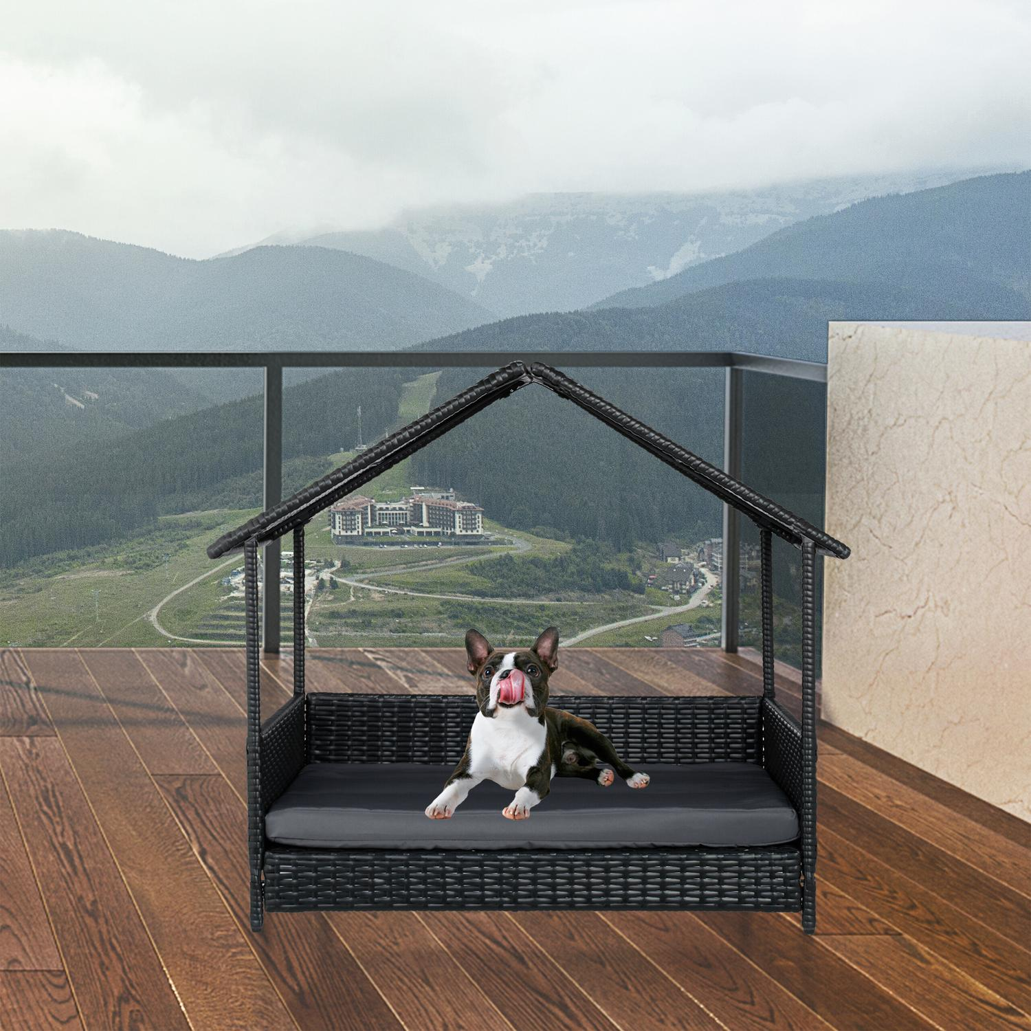 Un Boston Terrier se lame los labios en una cama para perros con techo en una terraza de madera.