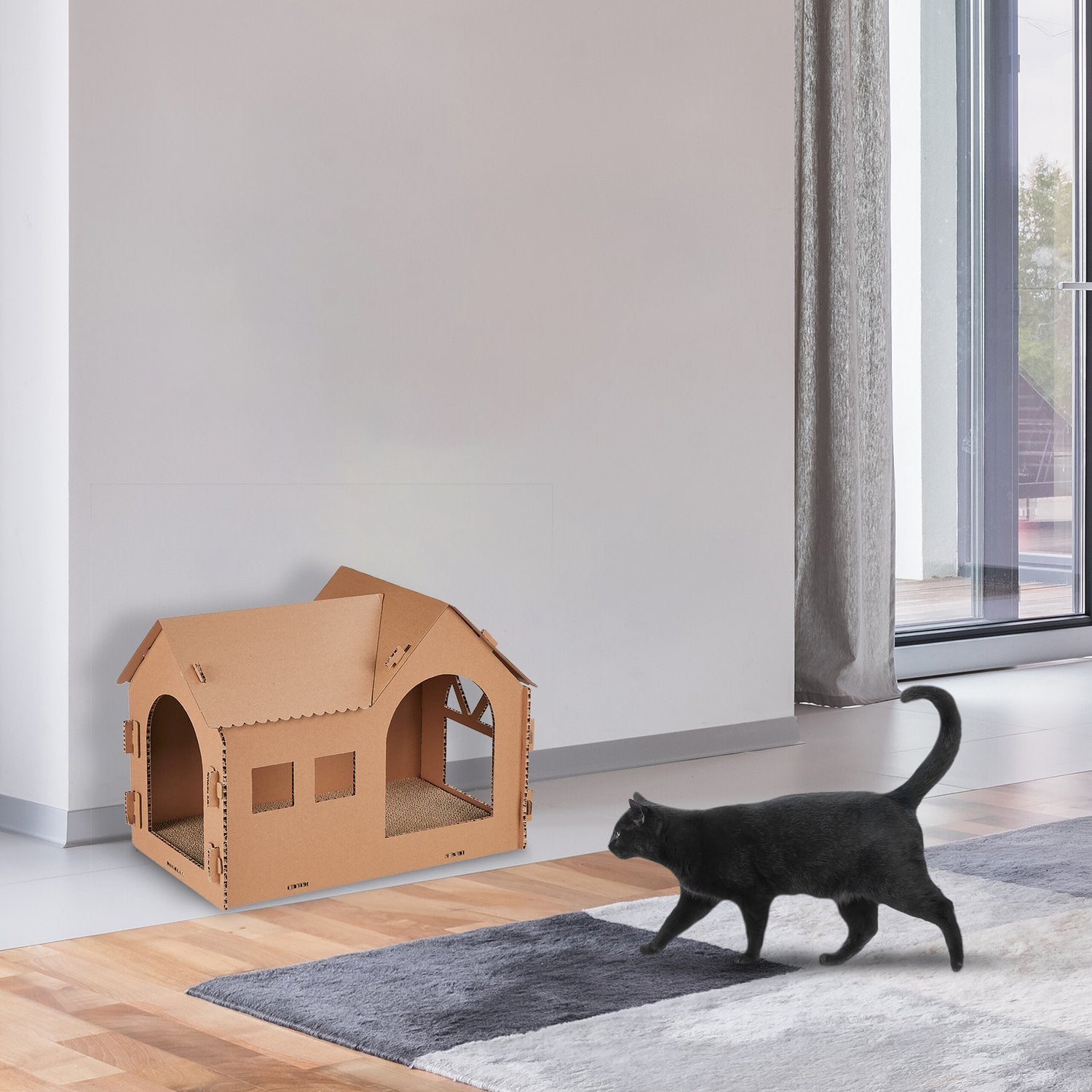 Un gato negro pasa junto a una casa de cartón sobre una alfombra.