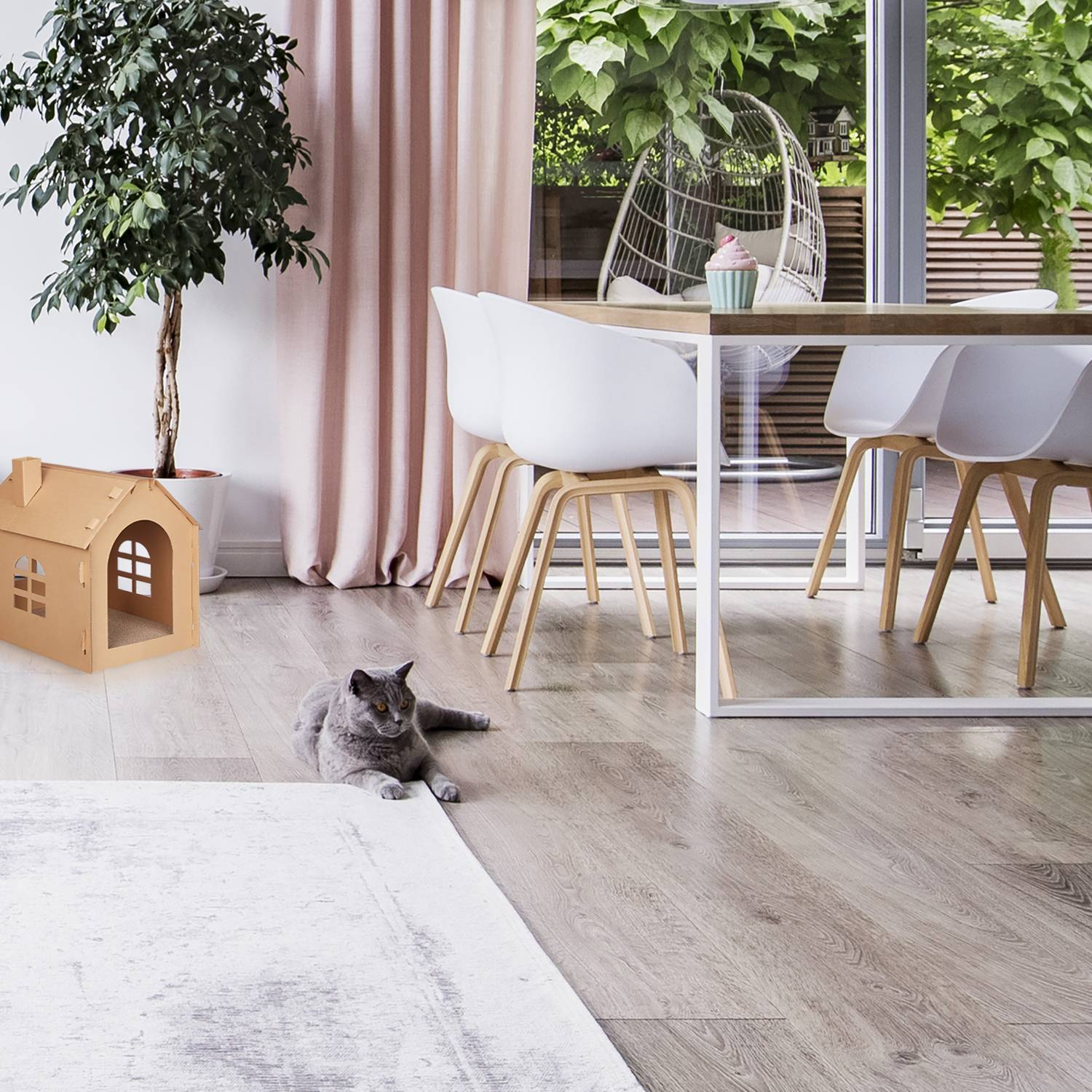 Un gato yace en el suelo junto a una casa de cartón y una alfombra.