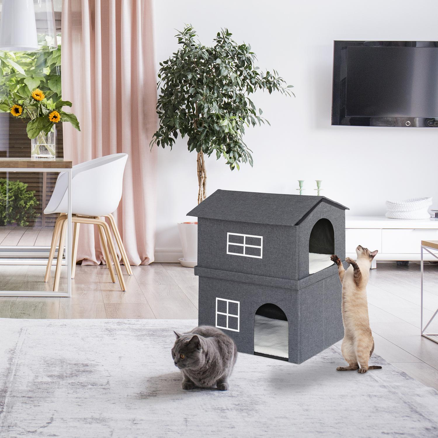 Dos gatos juegan en una sala de estar cerca de una casa para gatos de dos pisos.