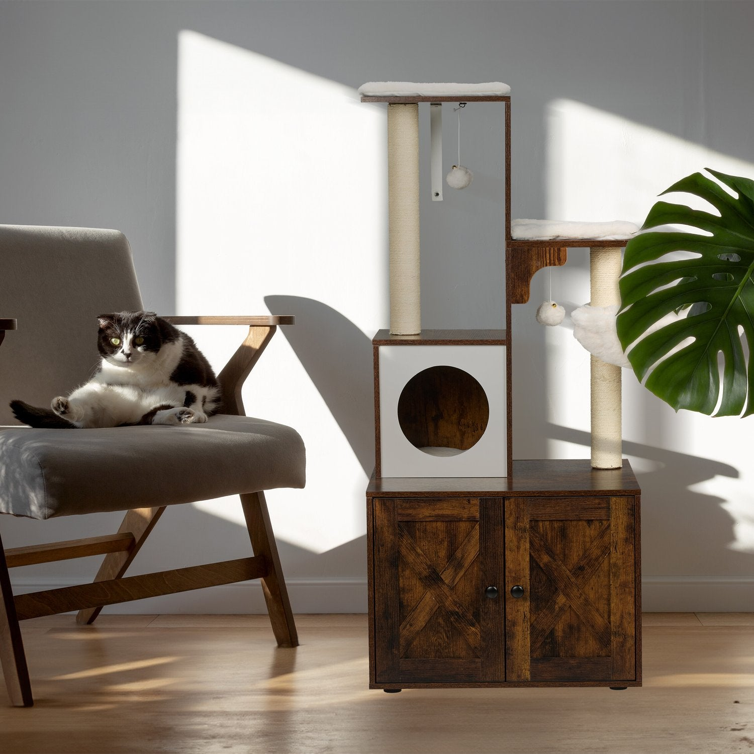 Un gato se sienta en un sillón junto a un rascador y una planta.