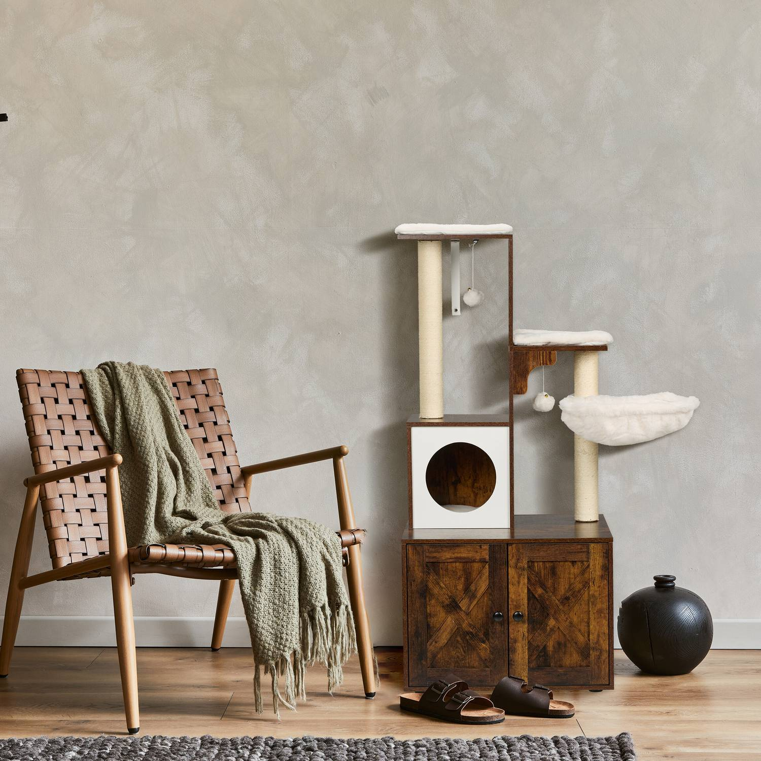 Una silla tejida marrón con manta verde junto a árbol para gatos y bola negra.