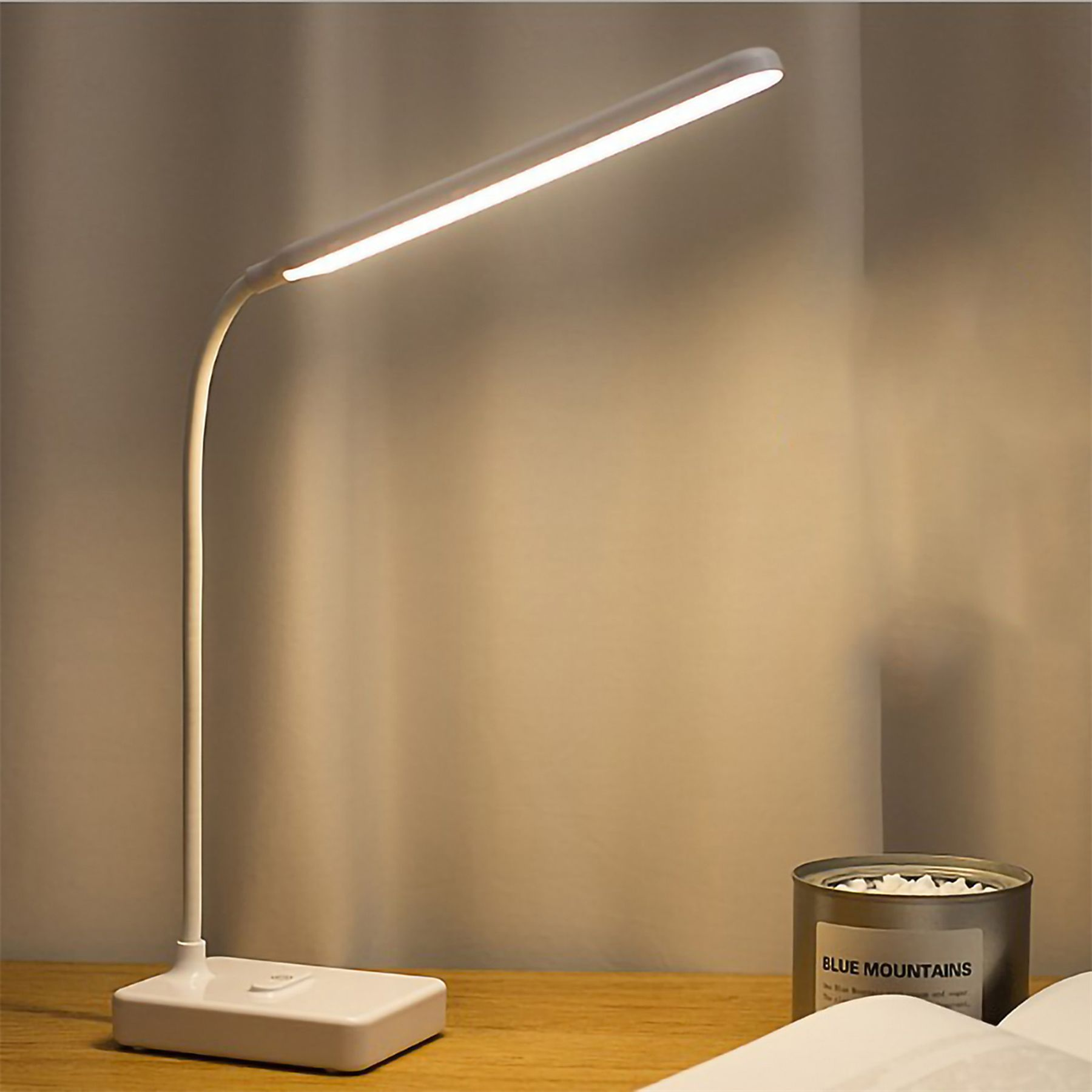 Eine weiße Schreibtischlampe mit LED-Licht leuchtet auf einem Holztisch.