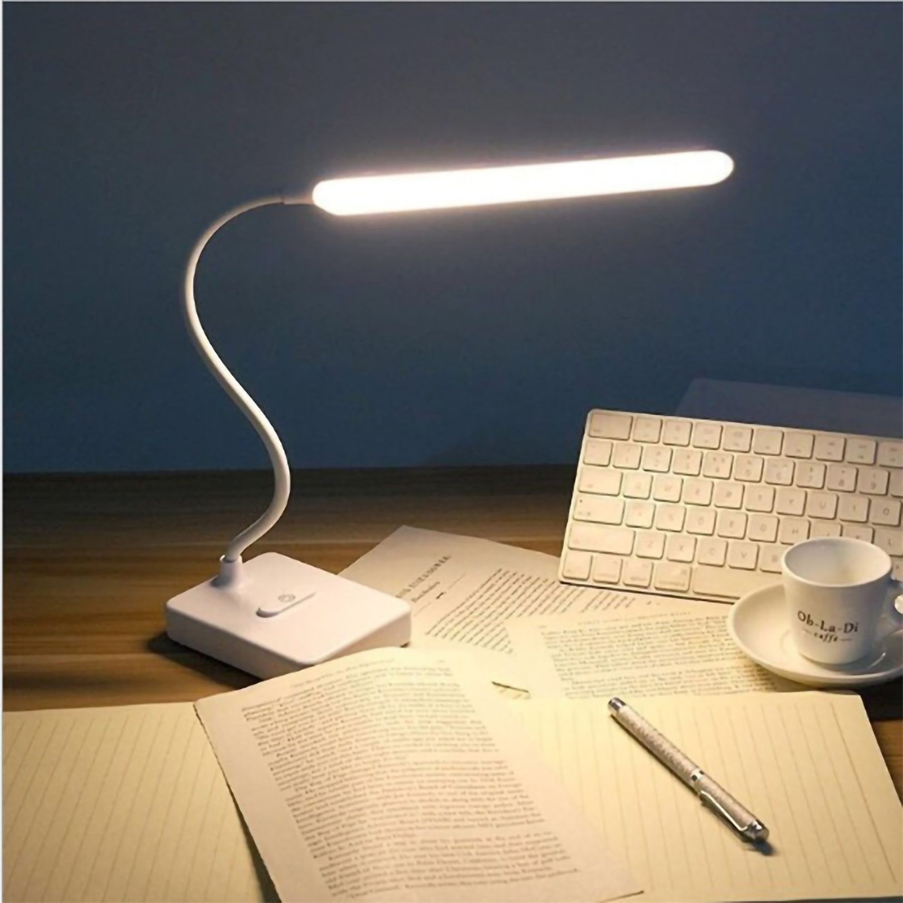 Eine weiße Schreibtischlampe leuchtet über einem Schreibtisch mit Tastatur und Notizbuch.