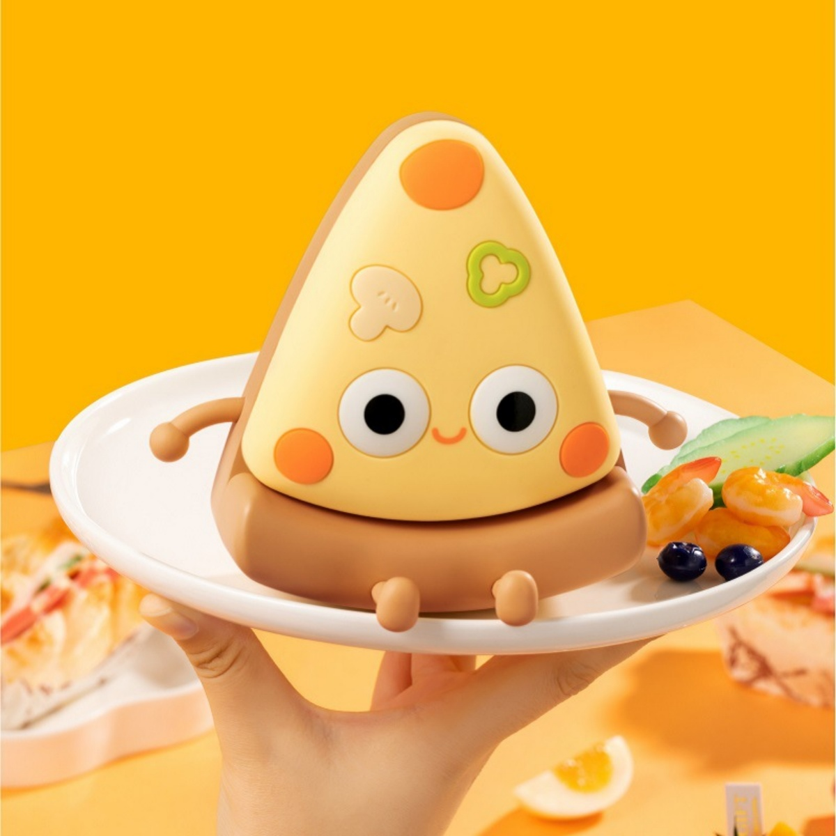 Eine Kawaii-Pizzafigur auf einem Teller mit Garnelen und Blaubeeren, vor orangem Hintergrund.