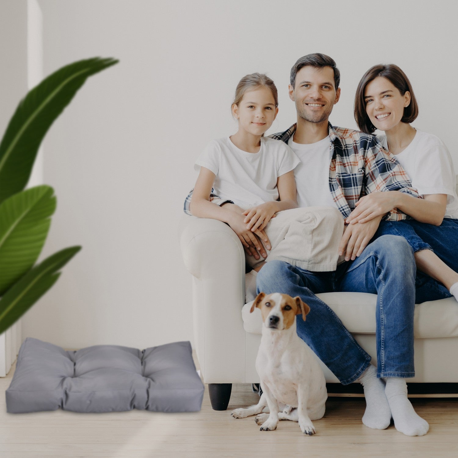 Familia con perro en sofá, cojín gris cerca.