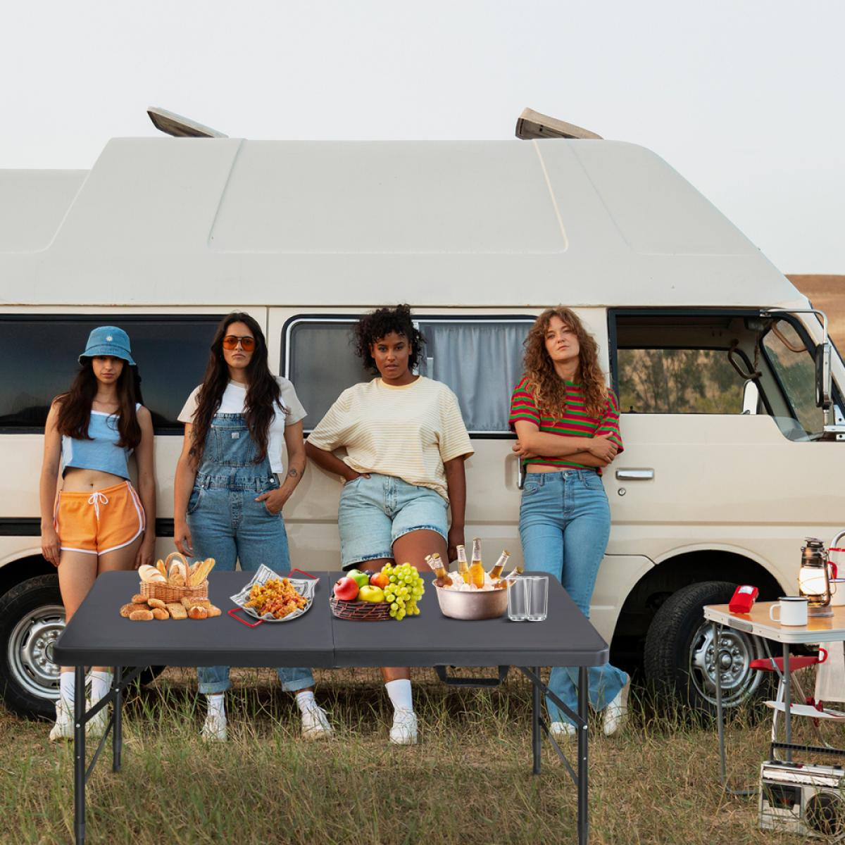 Vier Frauen stehen vor einem Wohnmobil mit einem Tisch voller Essen und Getränke.