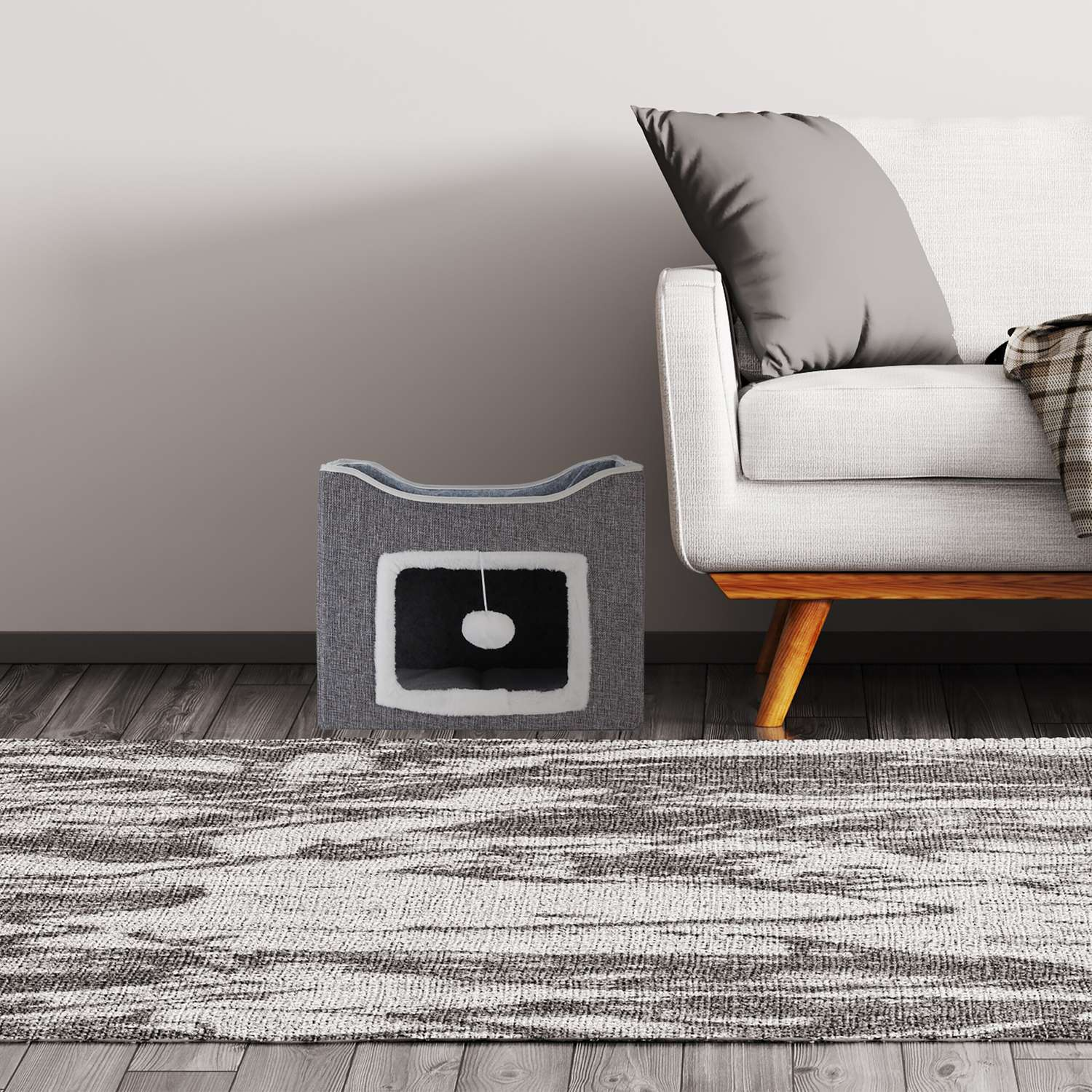 Casa de gato gris junto a sofá blanco, con alfombra delante.