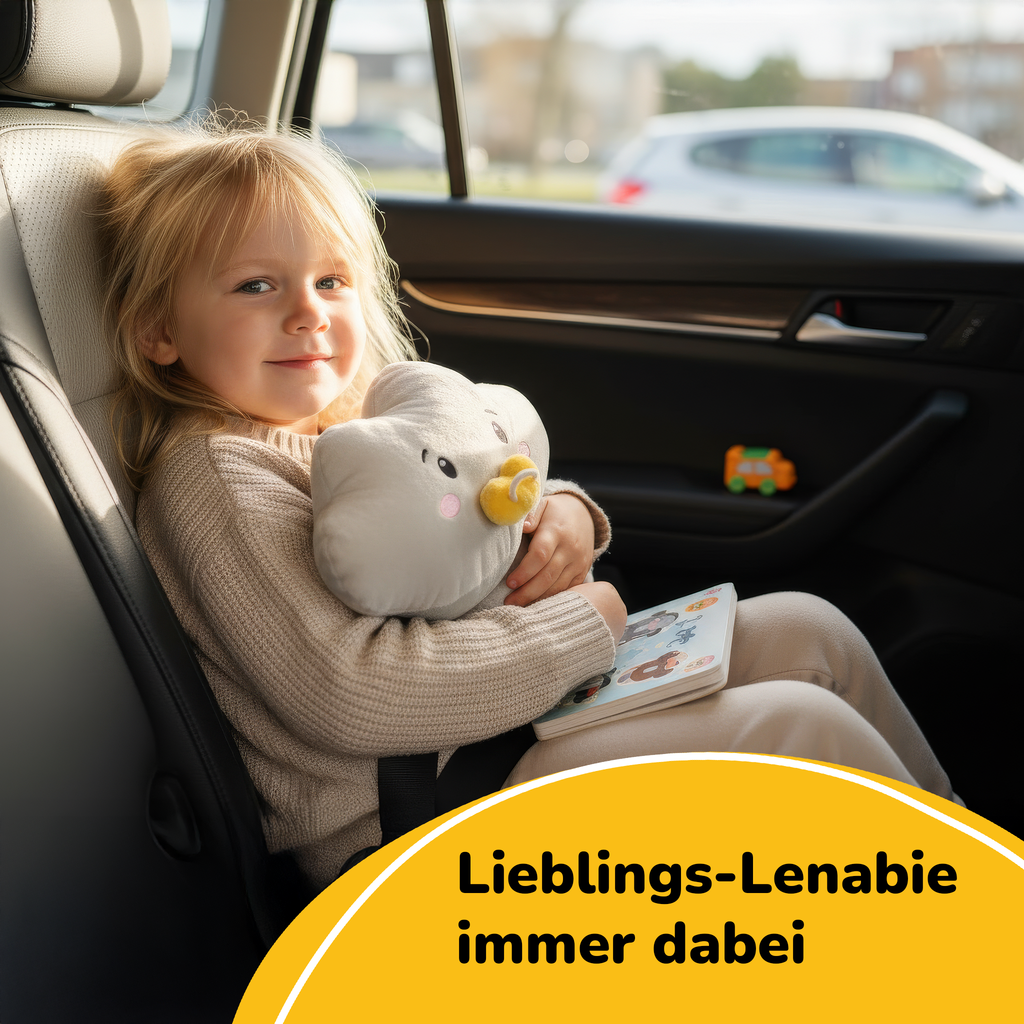 Una bambina bionda seduta in auto, tiene in braccio un peluche e un libro.