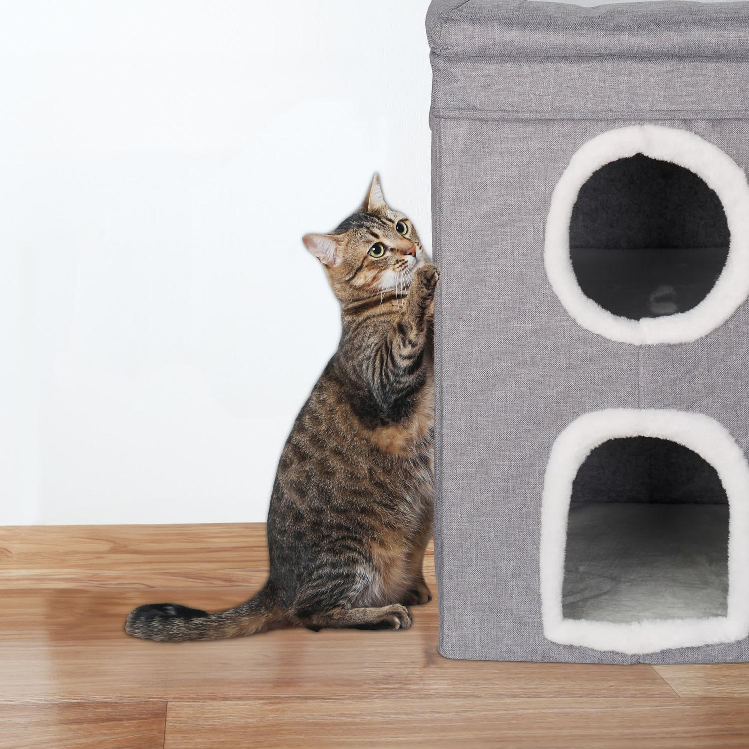 Un gato atigrado trepa a un árbol para gatos gris con dos aberturas.