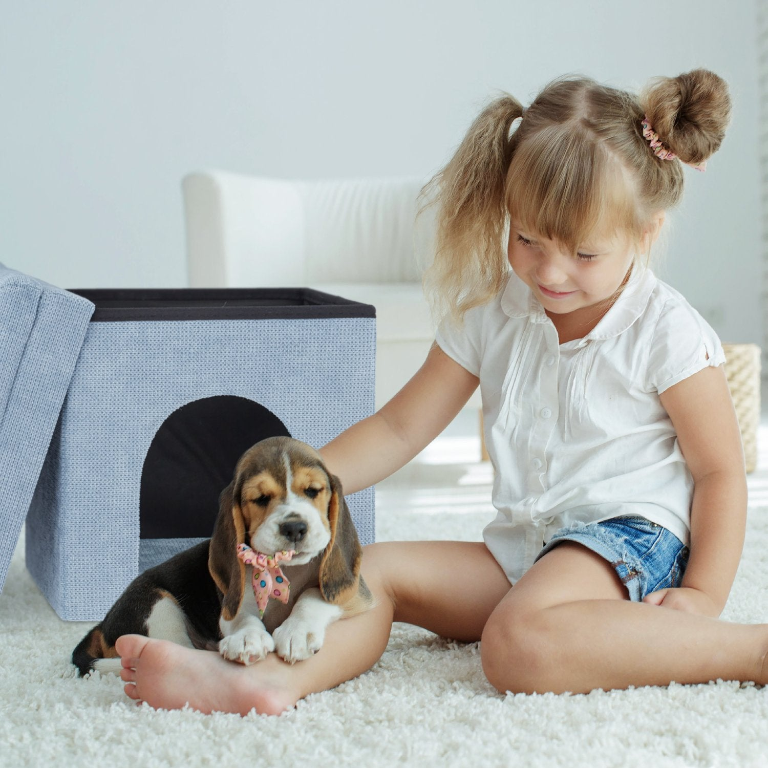 Un cachorro de beagle con un lazo se sienta en el regazo de una niña junto a una casa de juegos gris.