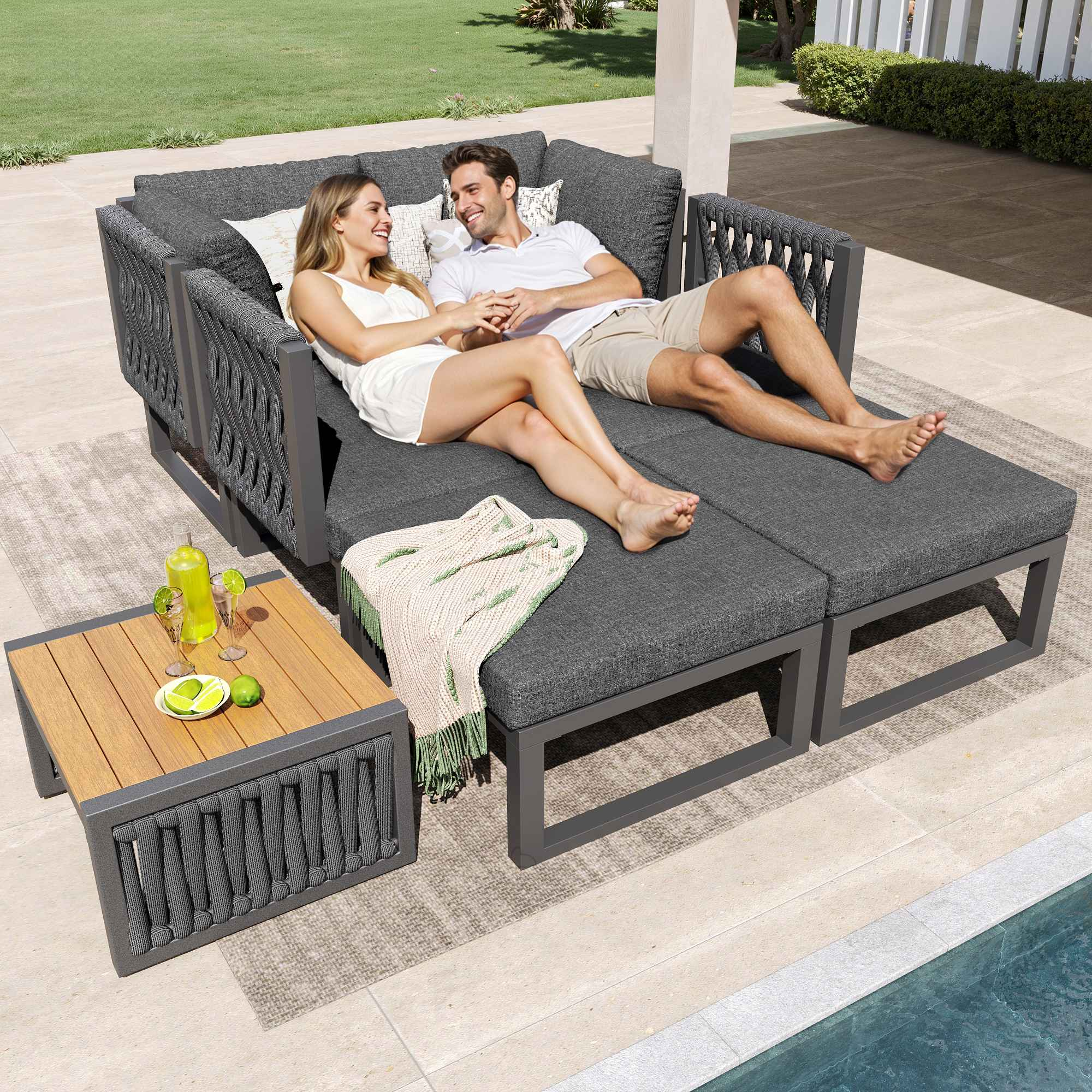 Ein Paar entspannt auf einem grauen Outdoor-Sofa neben einem Tisch mit Getränken.