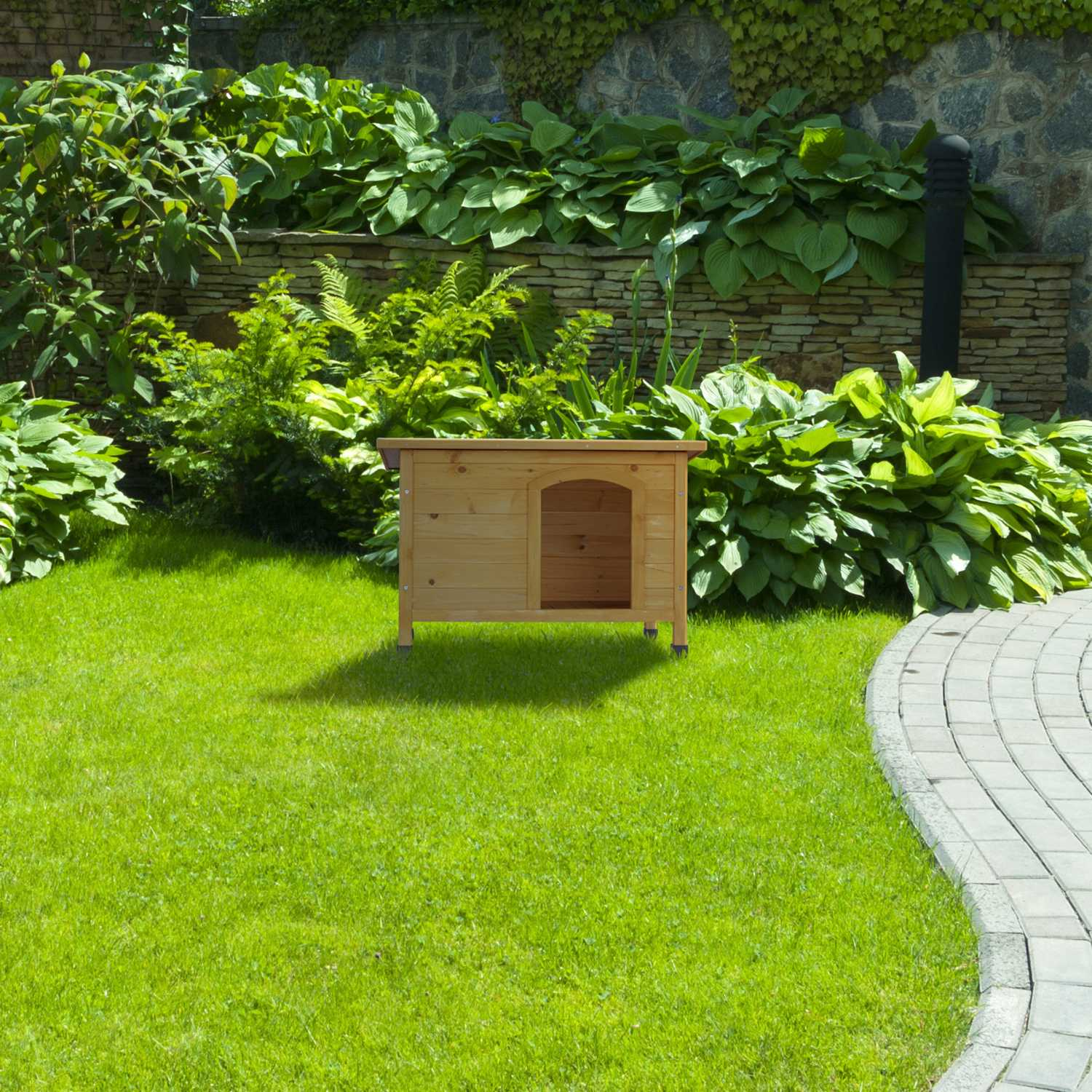 Caseta de perro de madera sobre césped verde con muro de piedra y plantas.