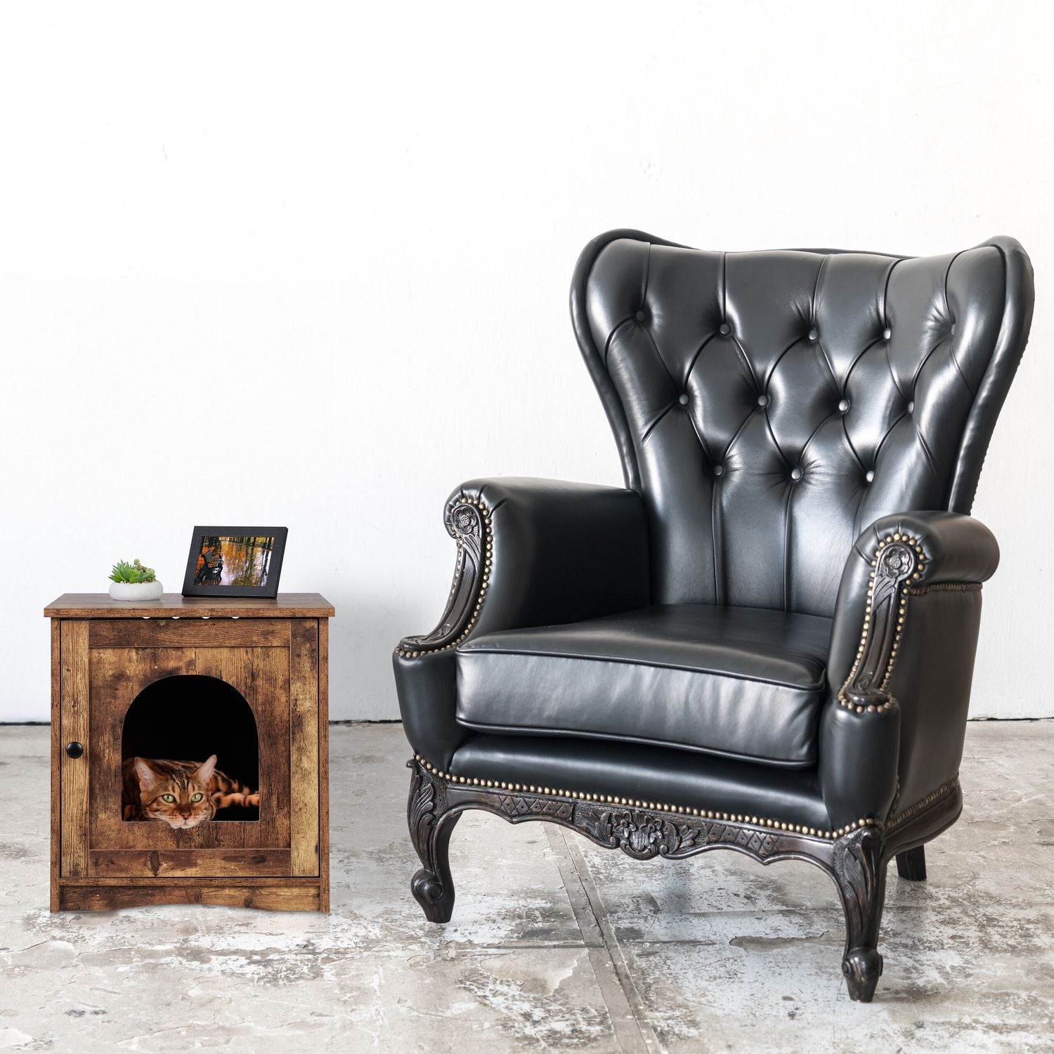 Una casa para gatos de armario de madera marrón junto a un sillón de cuero negro.