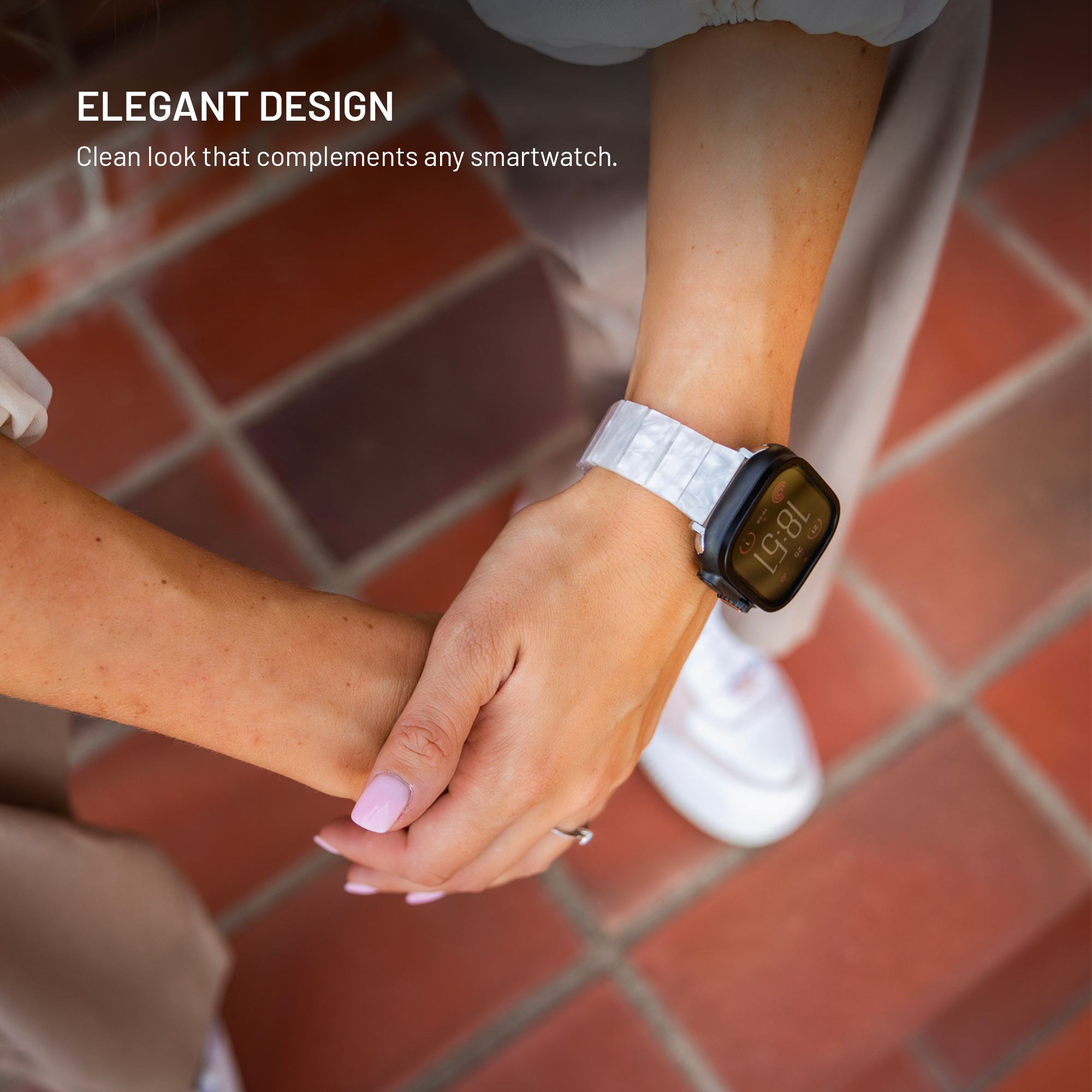 Nahaufnahme einer Hand mit einer Smartwatch mit weißem Armband auf einer Ziegelterrasse.