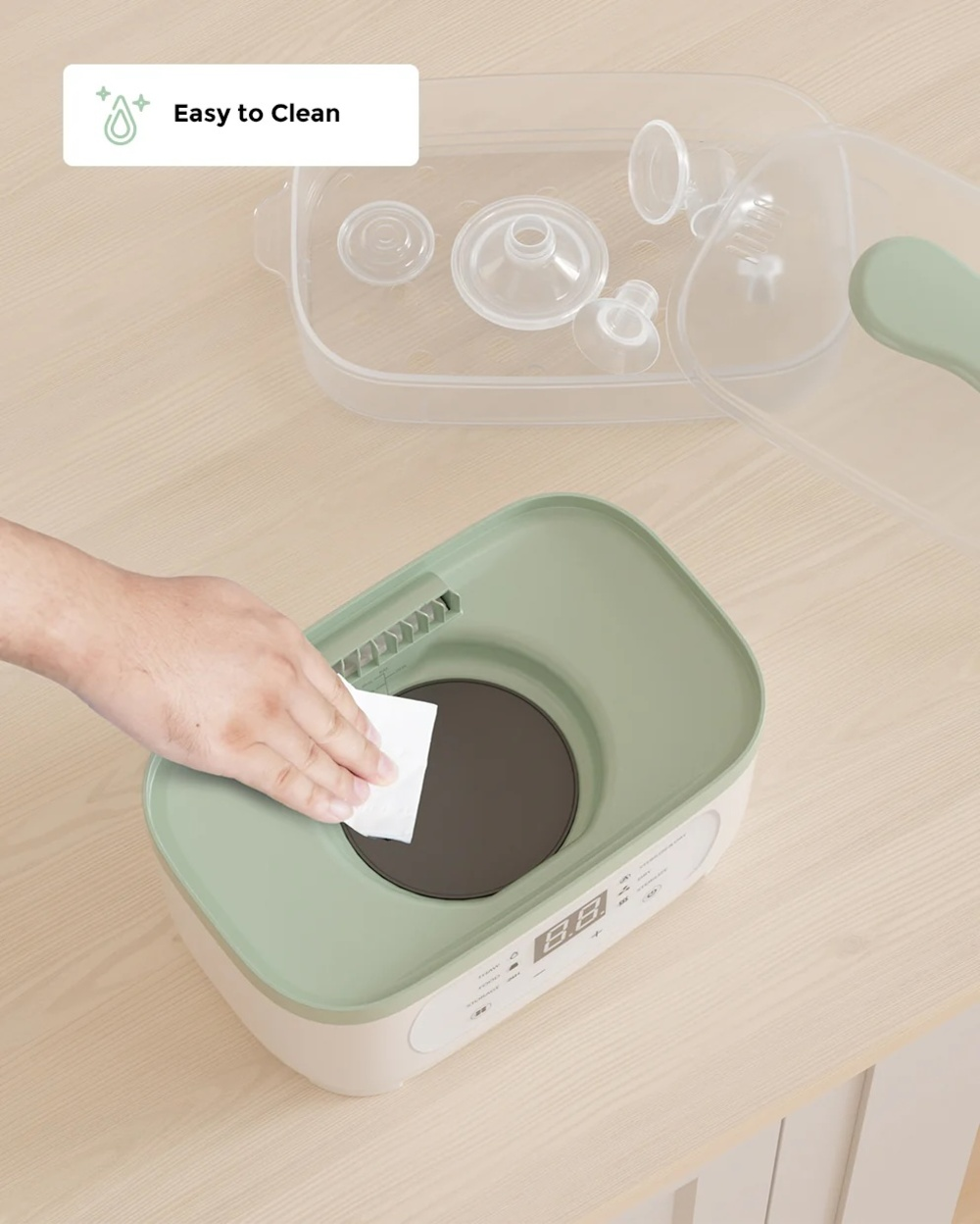 Eine Hand reinigt ein Gerät mit einem Tuch. Oben sind Babyflaschenteile.