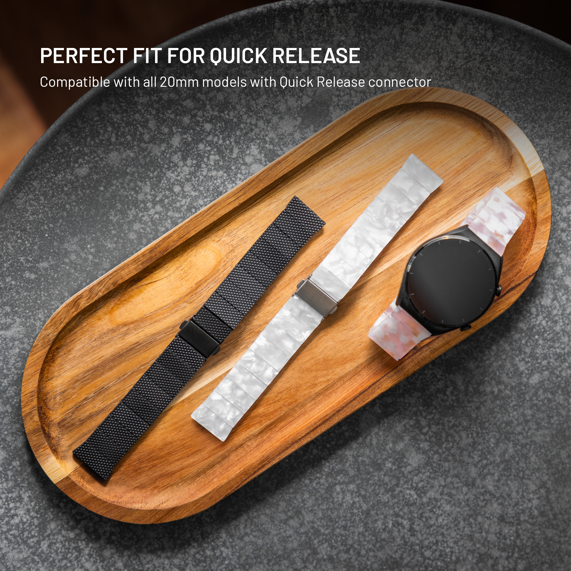 Ein schwarzes und ein weißes Uhrenarmband liegen auf einem Holztablett neben einer schwarzen Smartwatch.