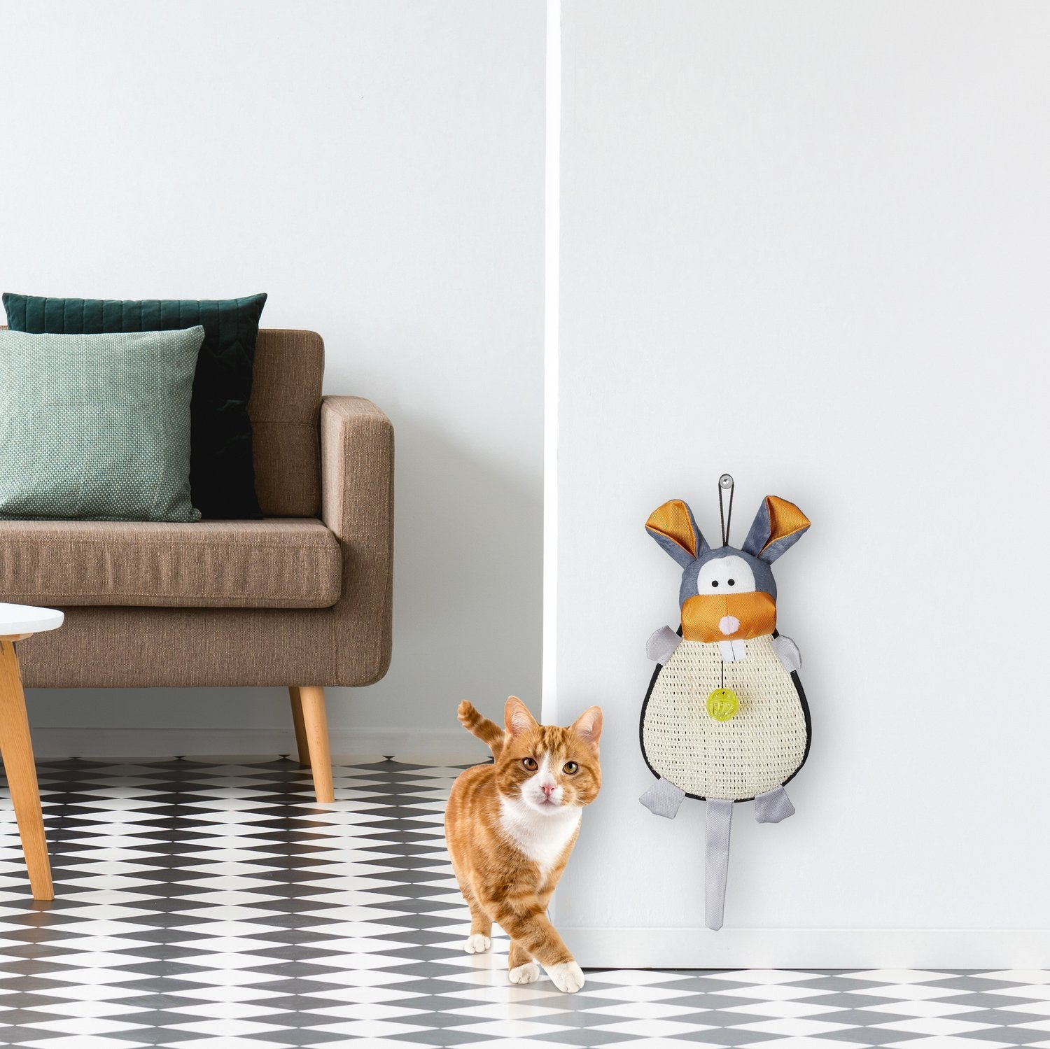 Un gato naranja se alza sobre un suelo blanco y negro junto a un rascador con forma de conejo.