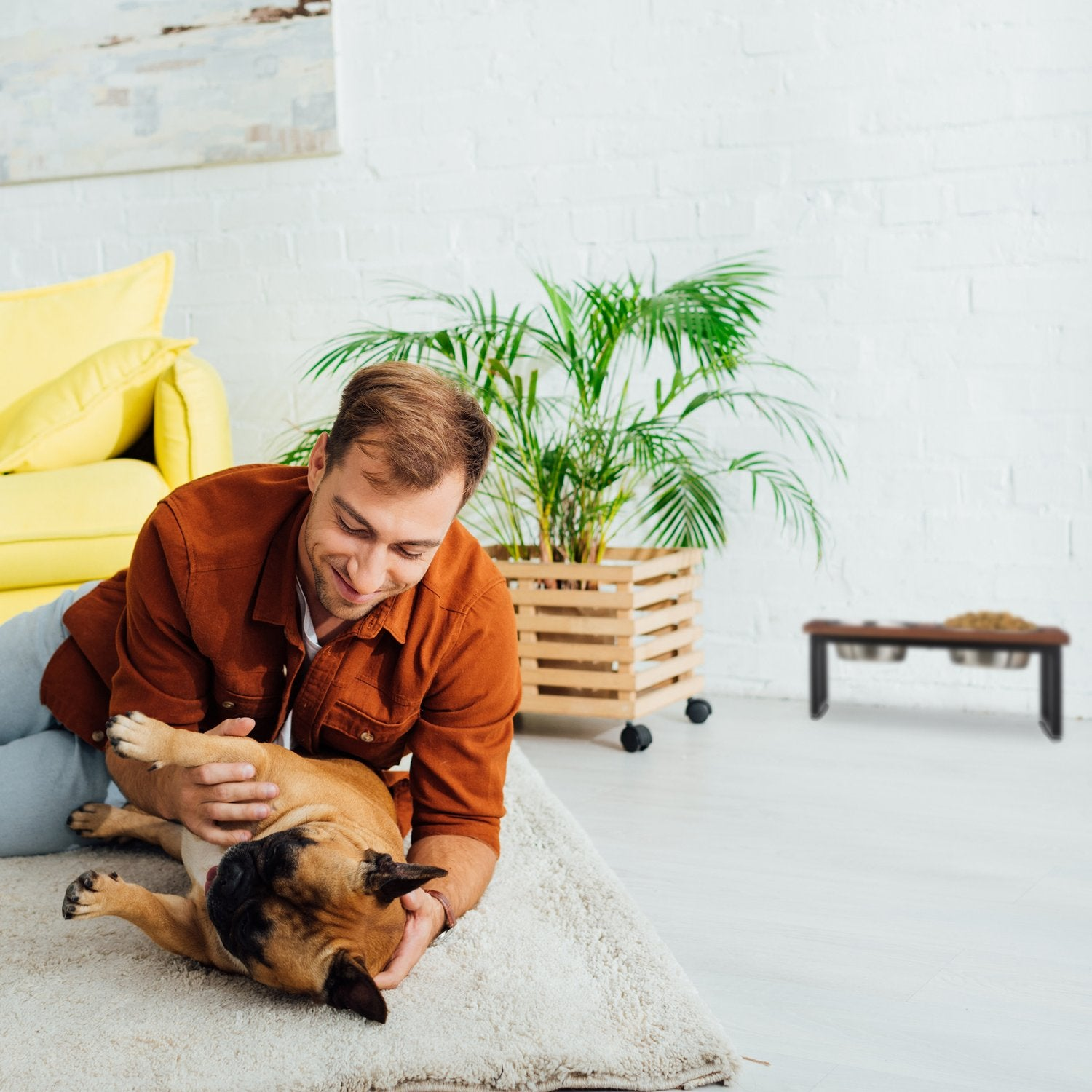 Un hombre con camisa marrón juega con un bulldog en una alfombra.