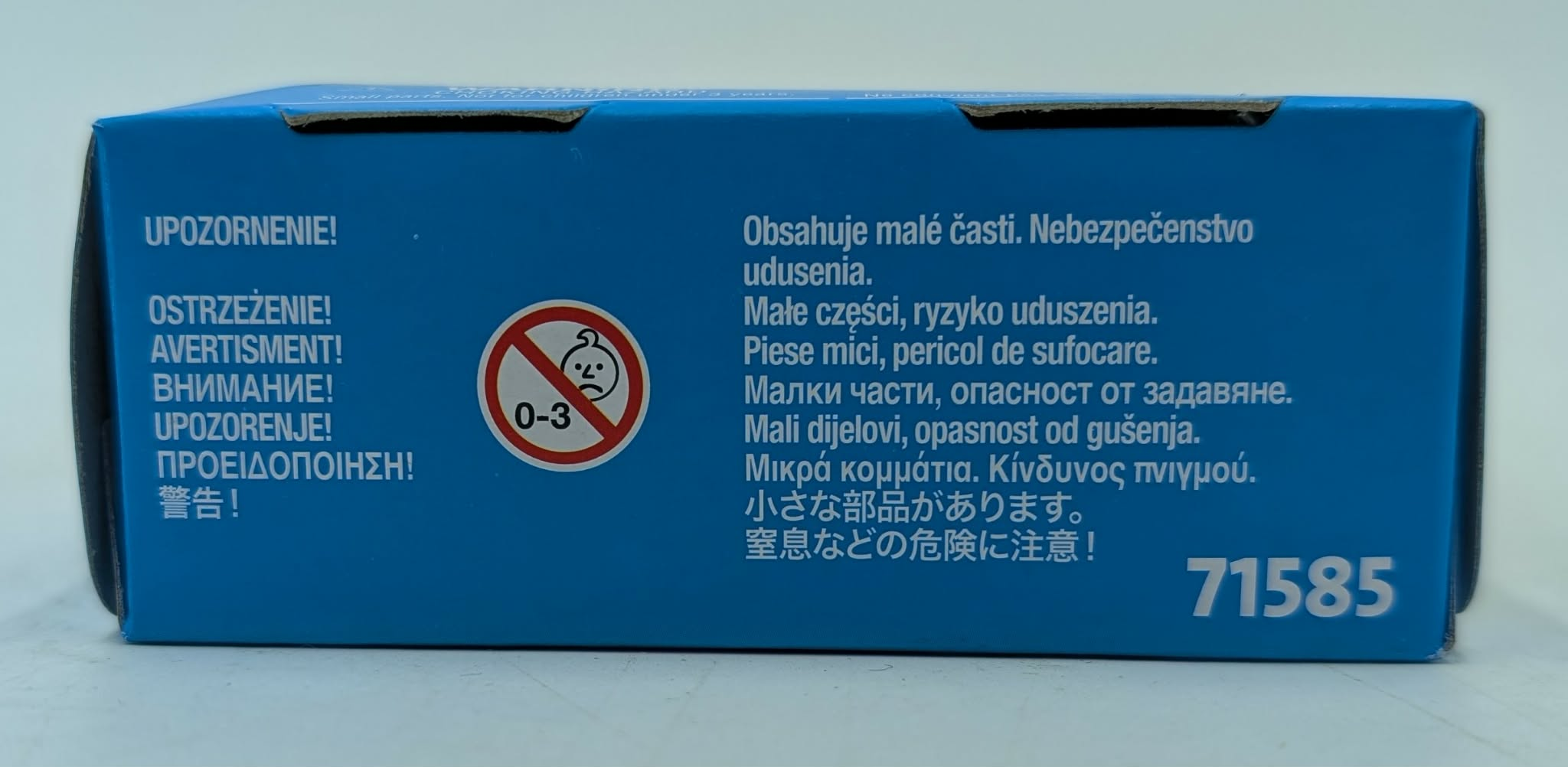 Scatola blu con avvisi multilingue e simbolo di età 0-3.
