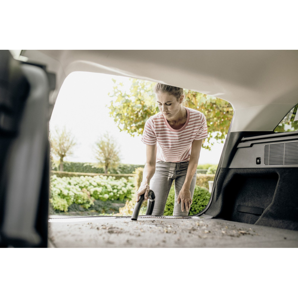 Kobieta odkurza bagażnik samochodu na zewnątrz.