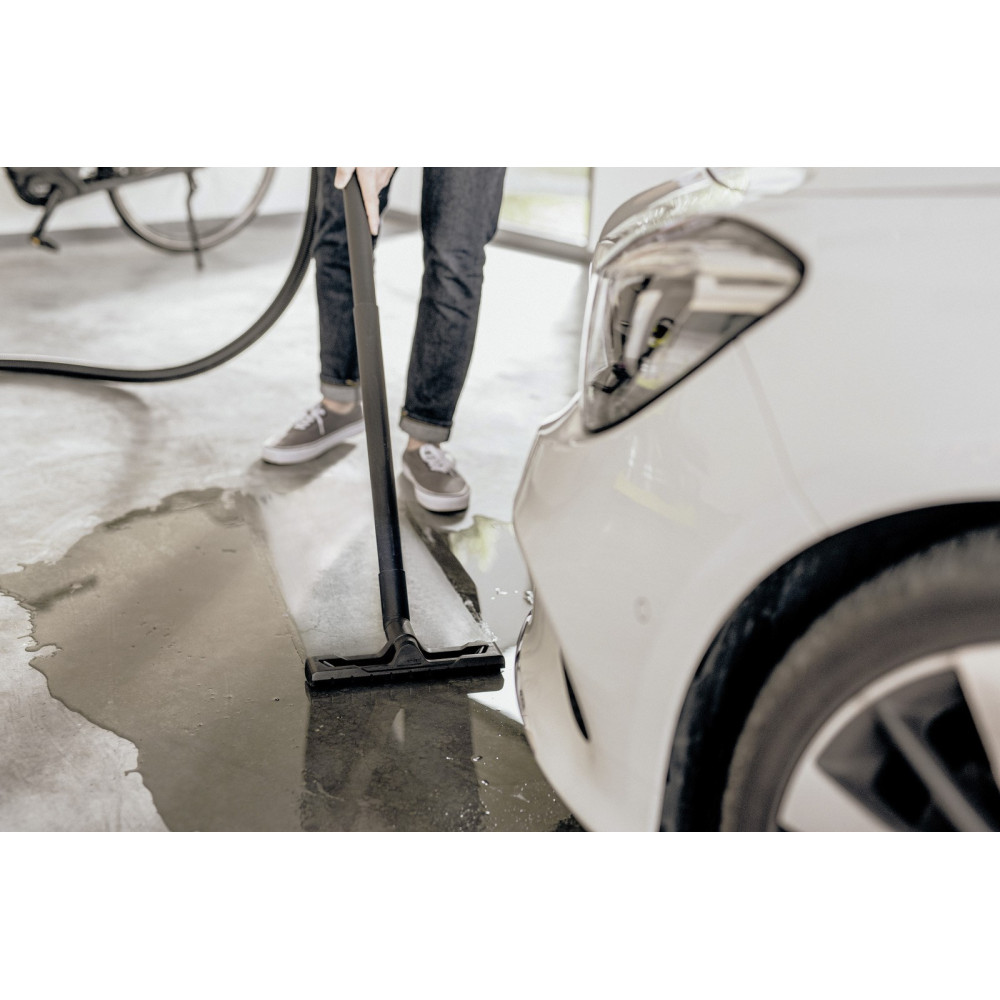 Osoba odkurza wodę z podłogi obok białego samochodu.