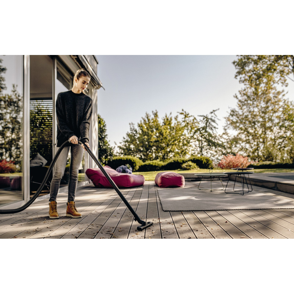 Kobieta odkurza drewniany taras z liśćmi i brudem.