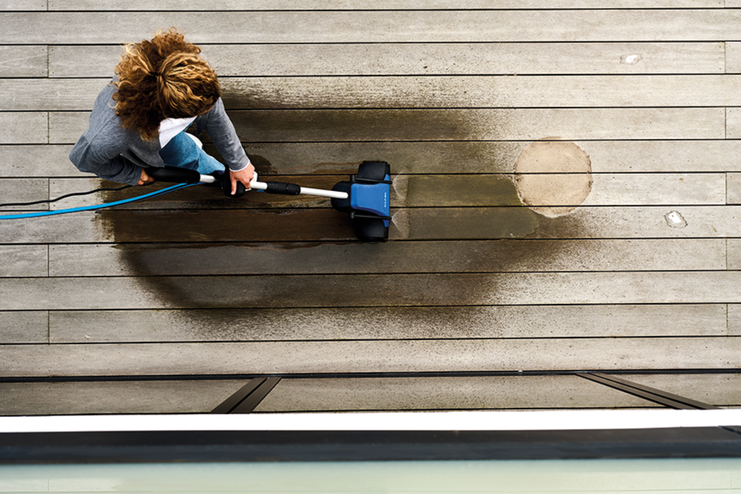 Person cleaning a wooden deck with a pressure washer.