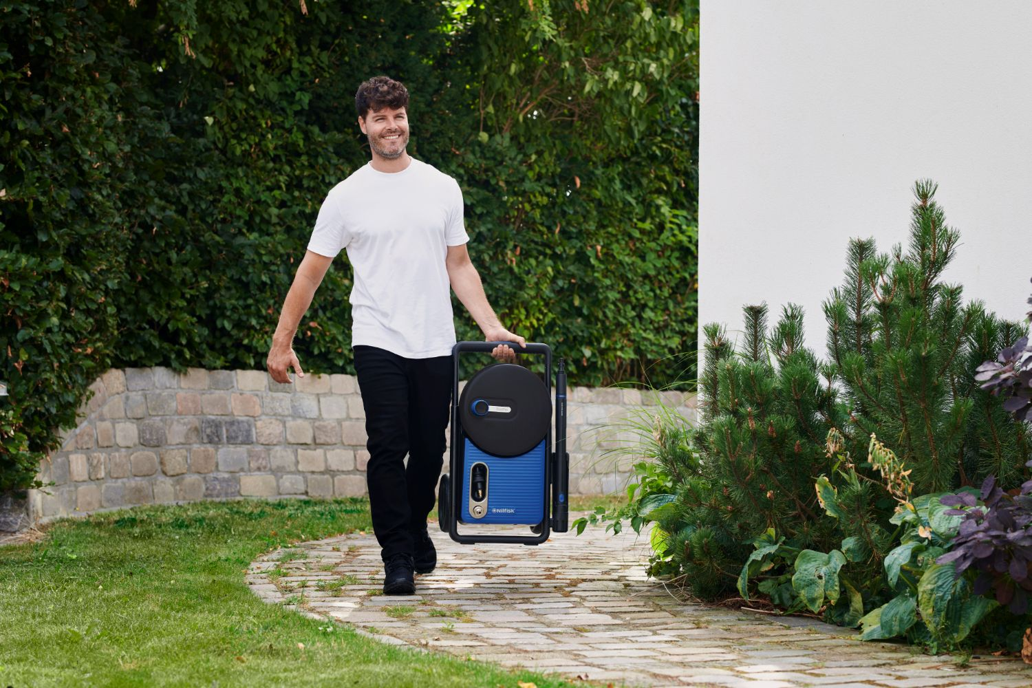 Man in white shirt carries blue pressure washer on a path.