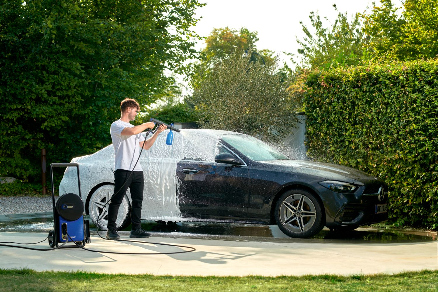 Man washes a dark car with a pressure washer and foam.