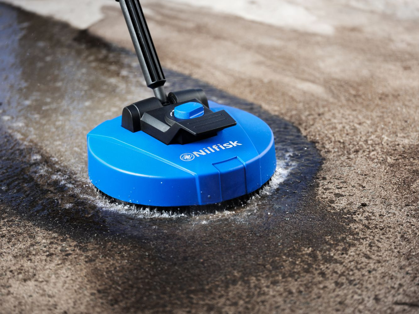 A blue Nilfisk floor cleaner with a black handle cleans a dirty floor.