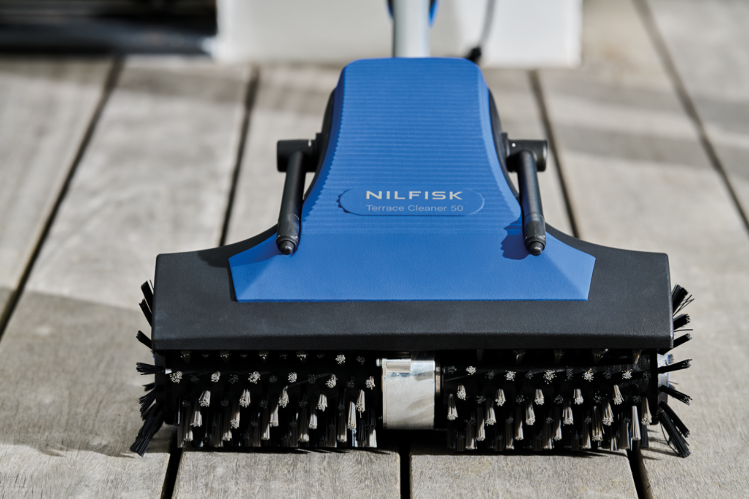 A blue Nilfisk terrace cleaner with brushes is on wooden planks.