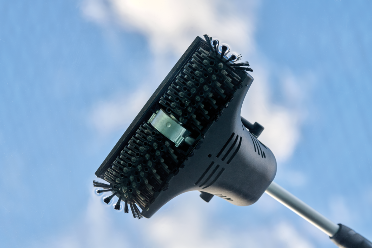 Black brush with handle against blue sky and clouds.