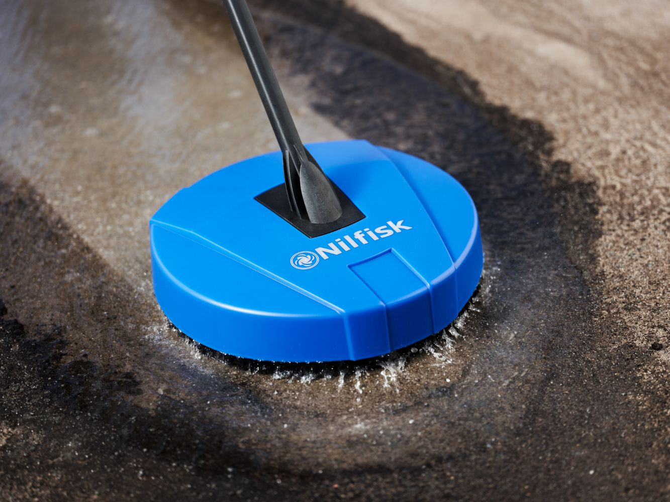 Blue Nilfisk brush cleaning wet ground with water spray.
