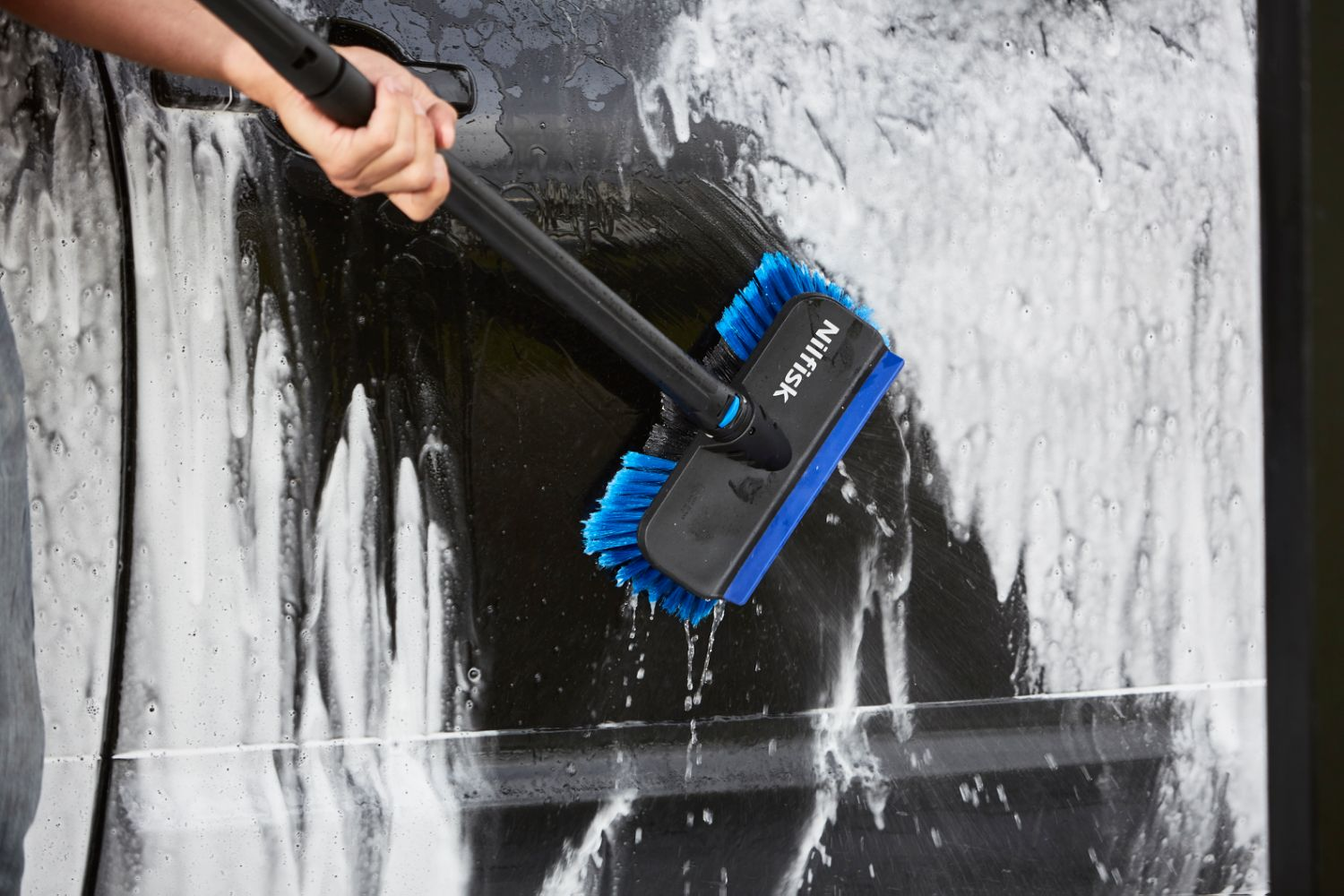 Person washing black car with blue and black brush and foam.