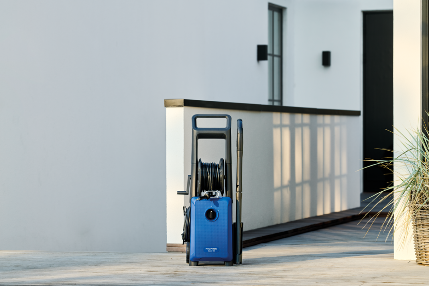 Ein blauer Hochdruckreiniger steht auf einem Betonboden vor einem weißen Gebäude.